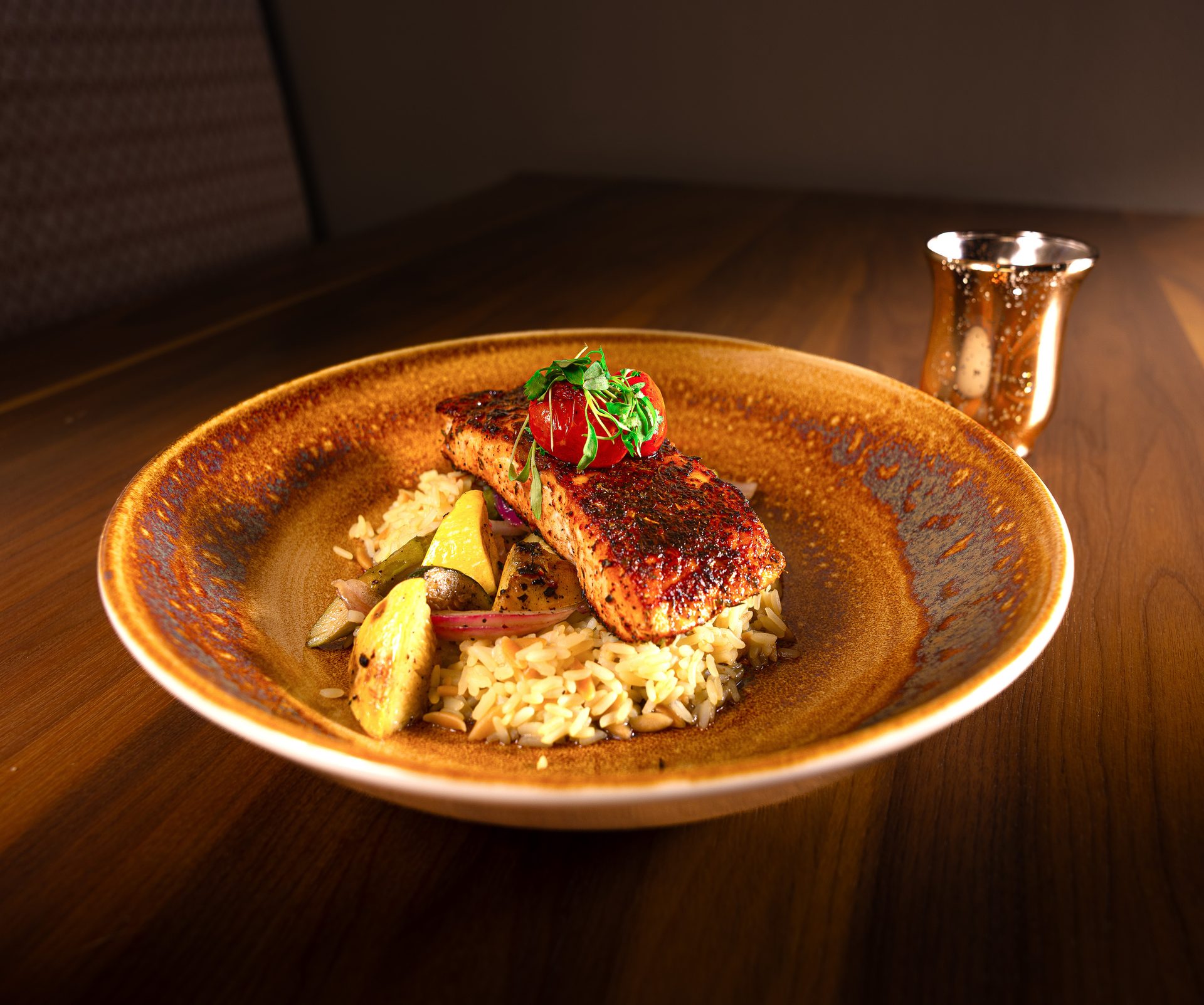 Spiced salmon fillet on rice with roasted vegetables and a tomato garnish, on a rustic plate.