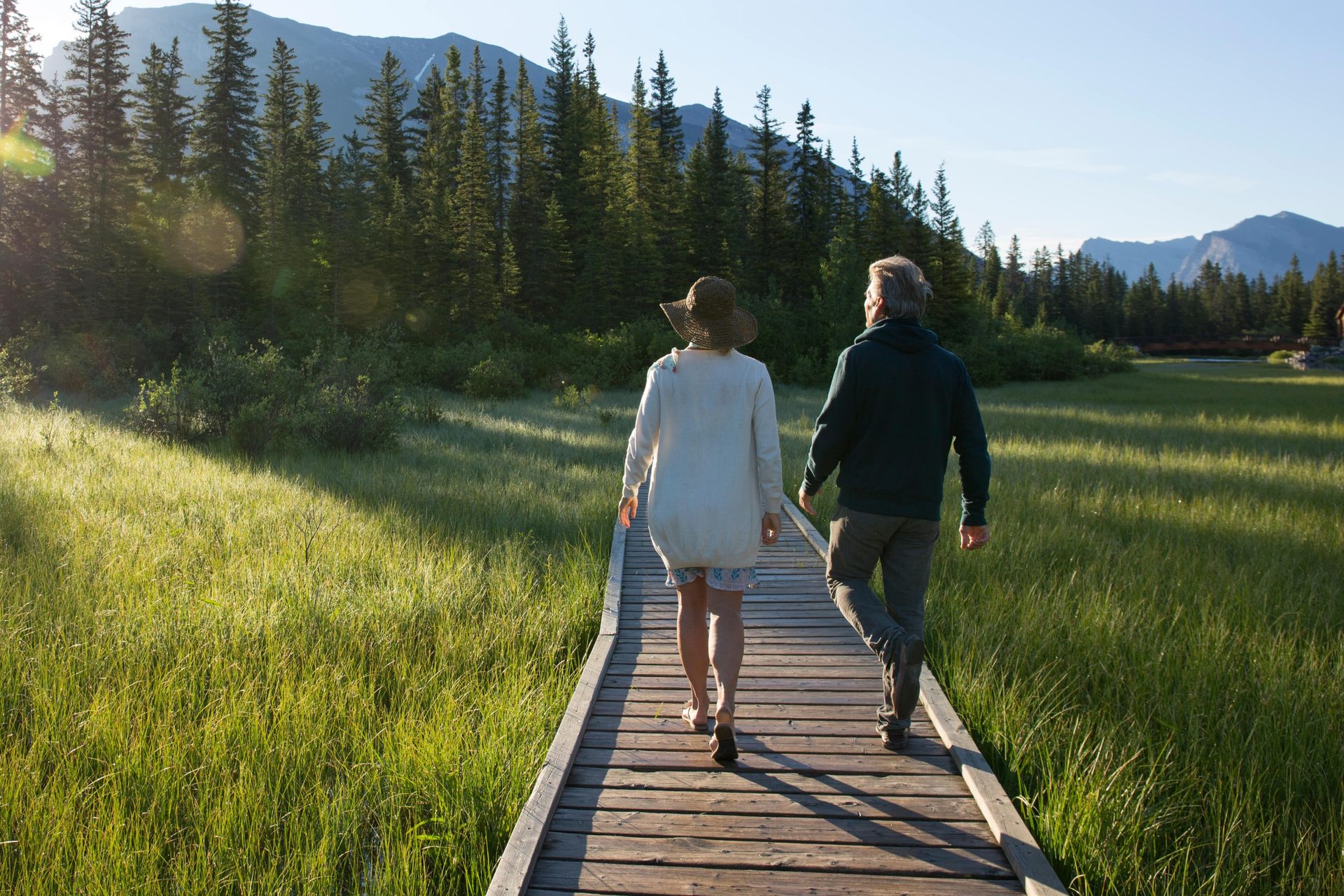 Two people walk on a boardwalk in a mountain meadow.