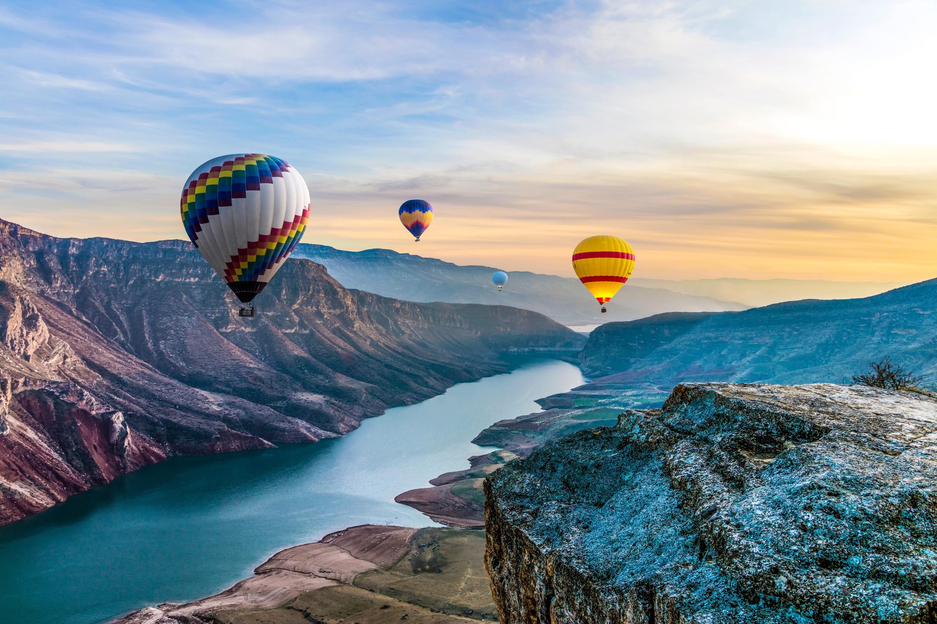 Hot air balloons float over a vast river canyon at sunset.