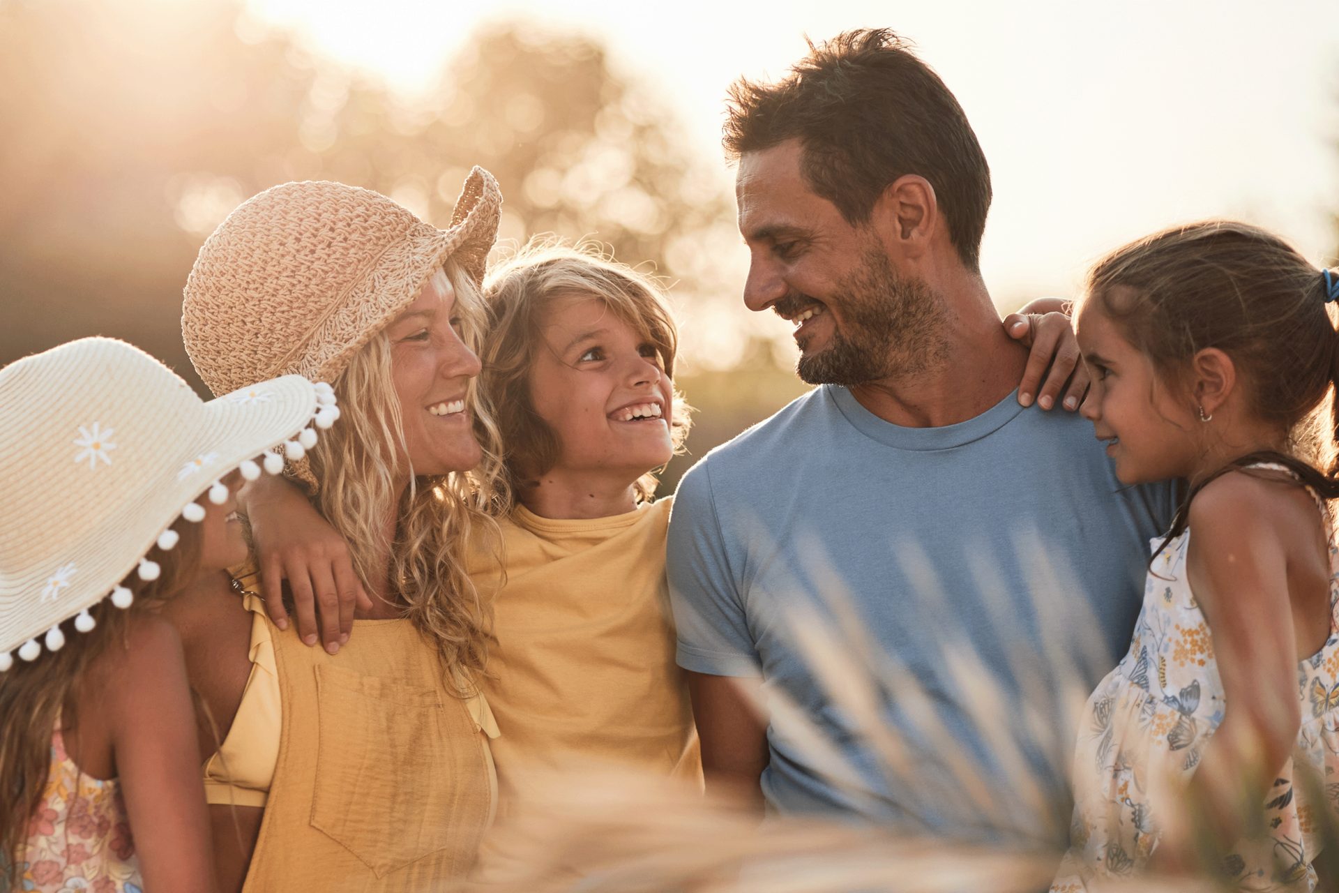 Happy family of four smiling outdoors at sunset.