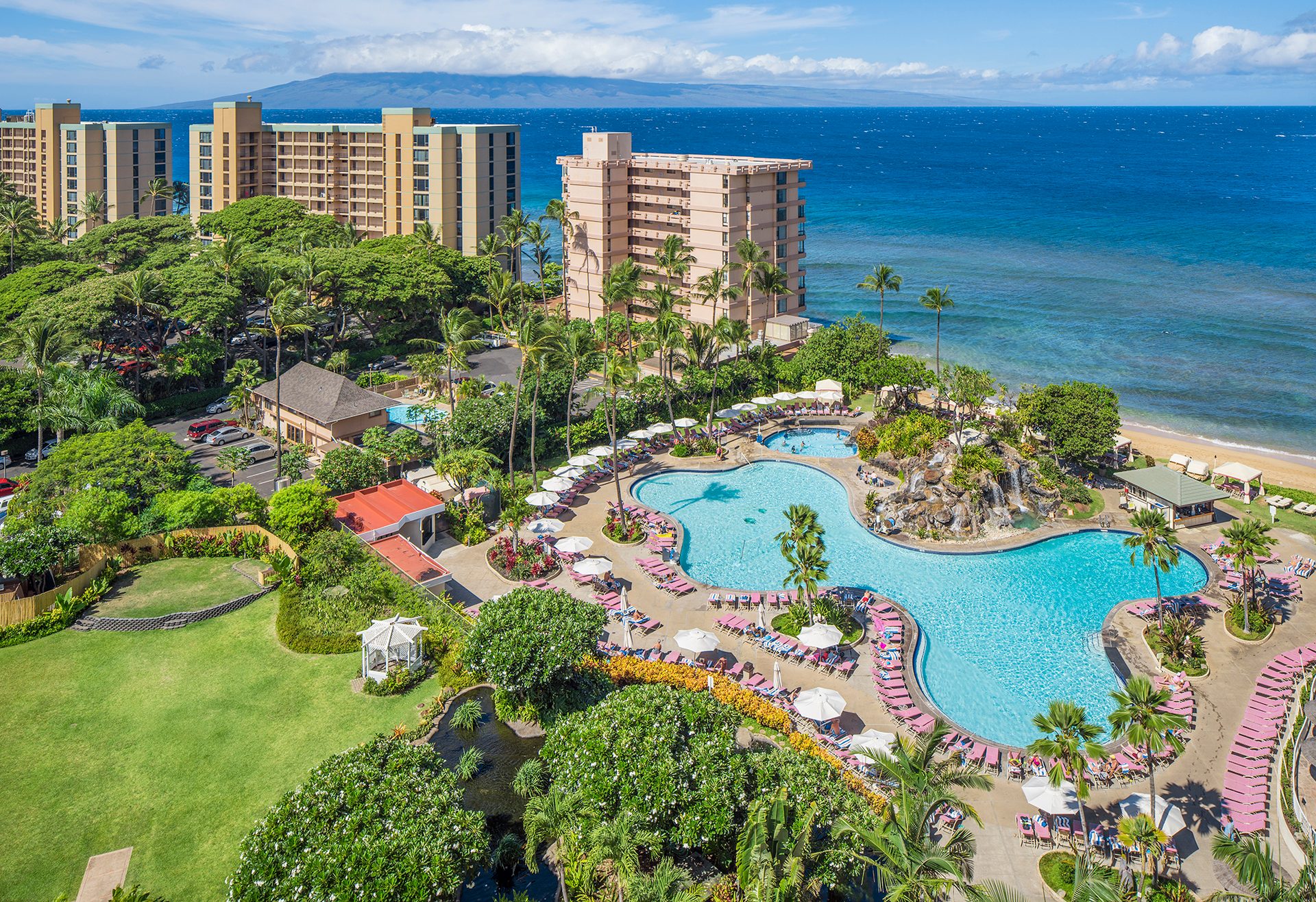Aerial view of a tropical resort with large pool, beach, and buildings.