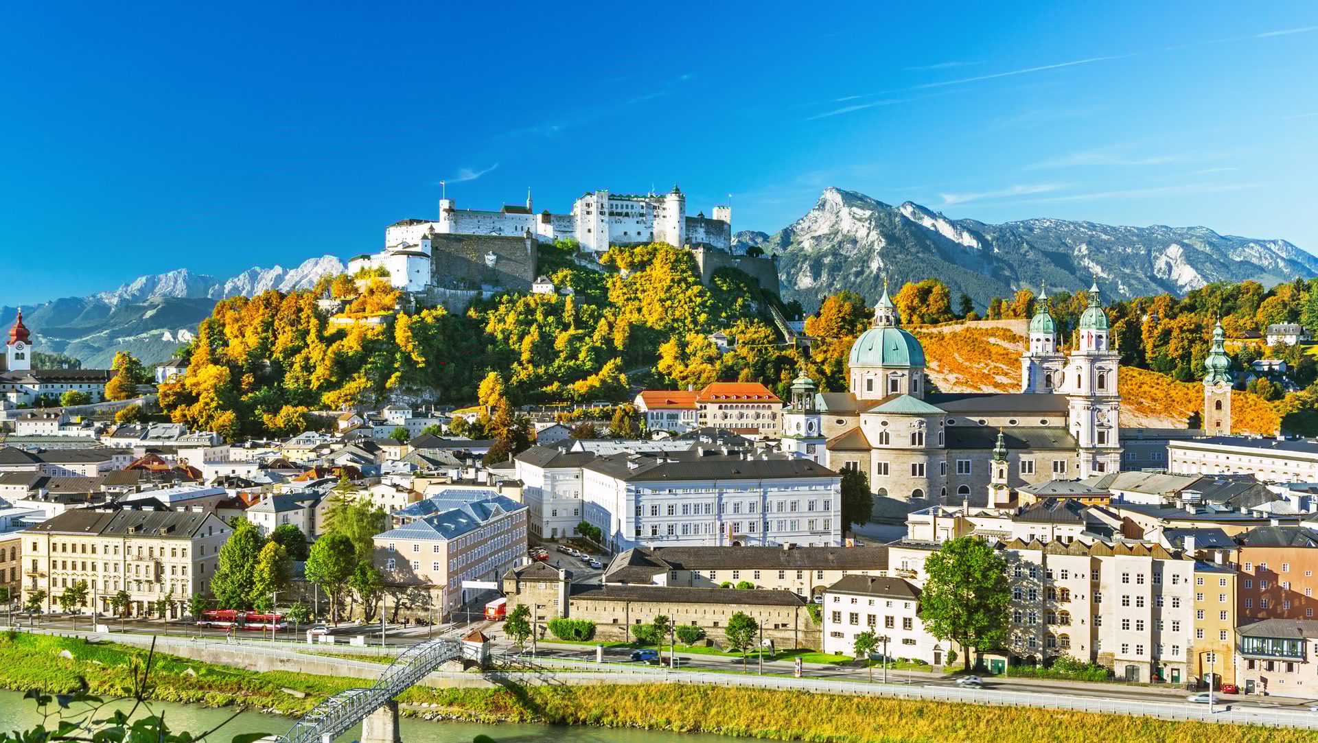 Panoramic view of Salzburg with fortress, cathedral, river, and autumn mountains.