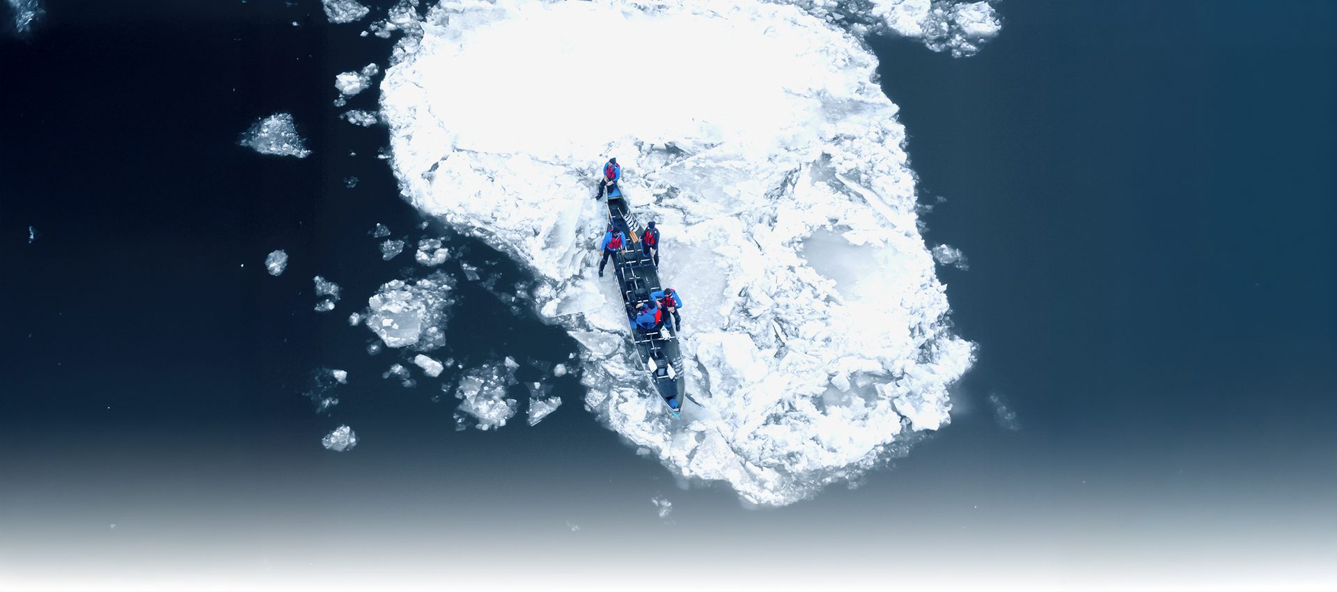 Aerial: People in a boat navigating large ice floes on dark water.