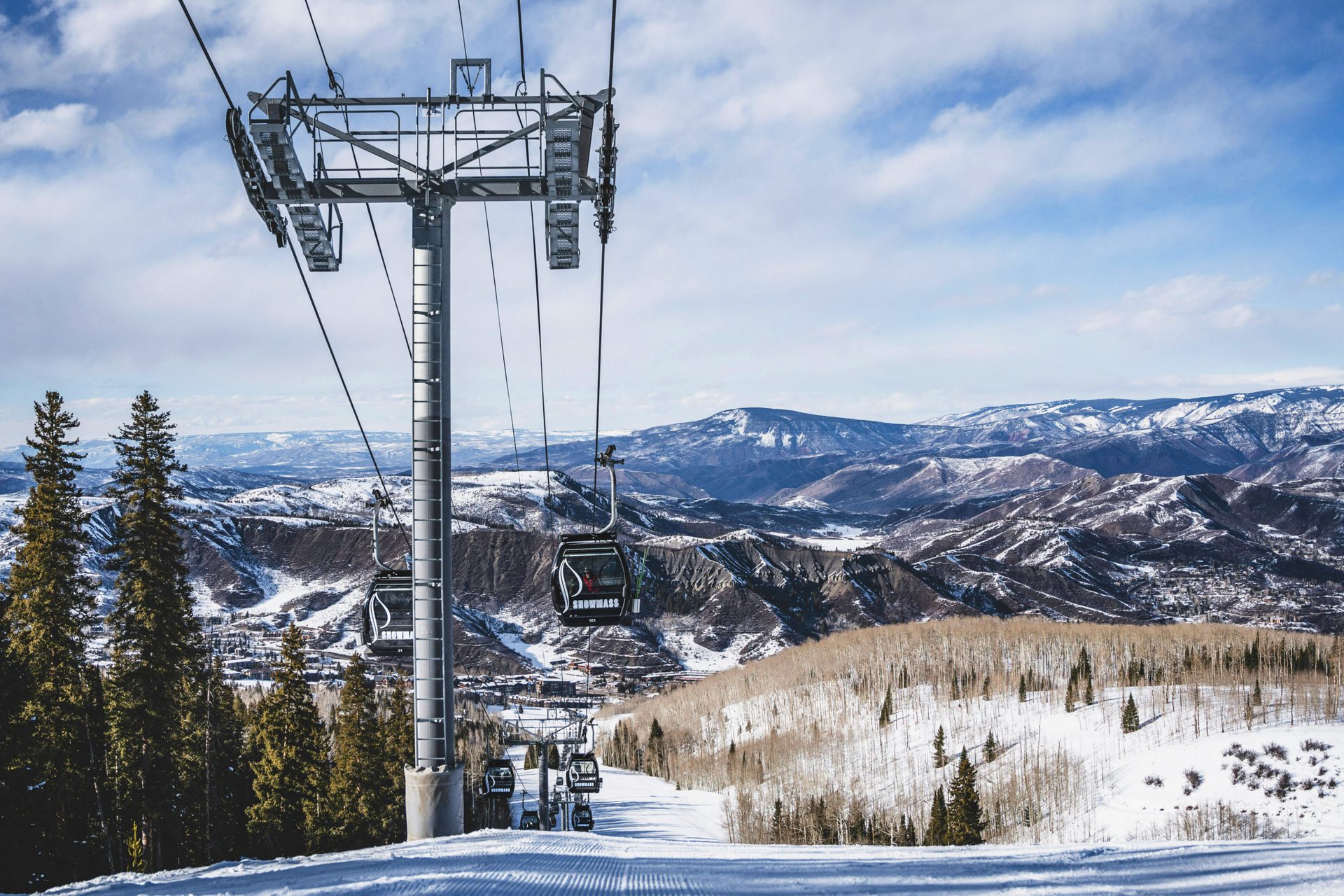 Snowmass ski resort: Gondolas on a ski lift, snowy mountains, and evergreen trees.