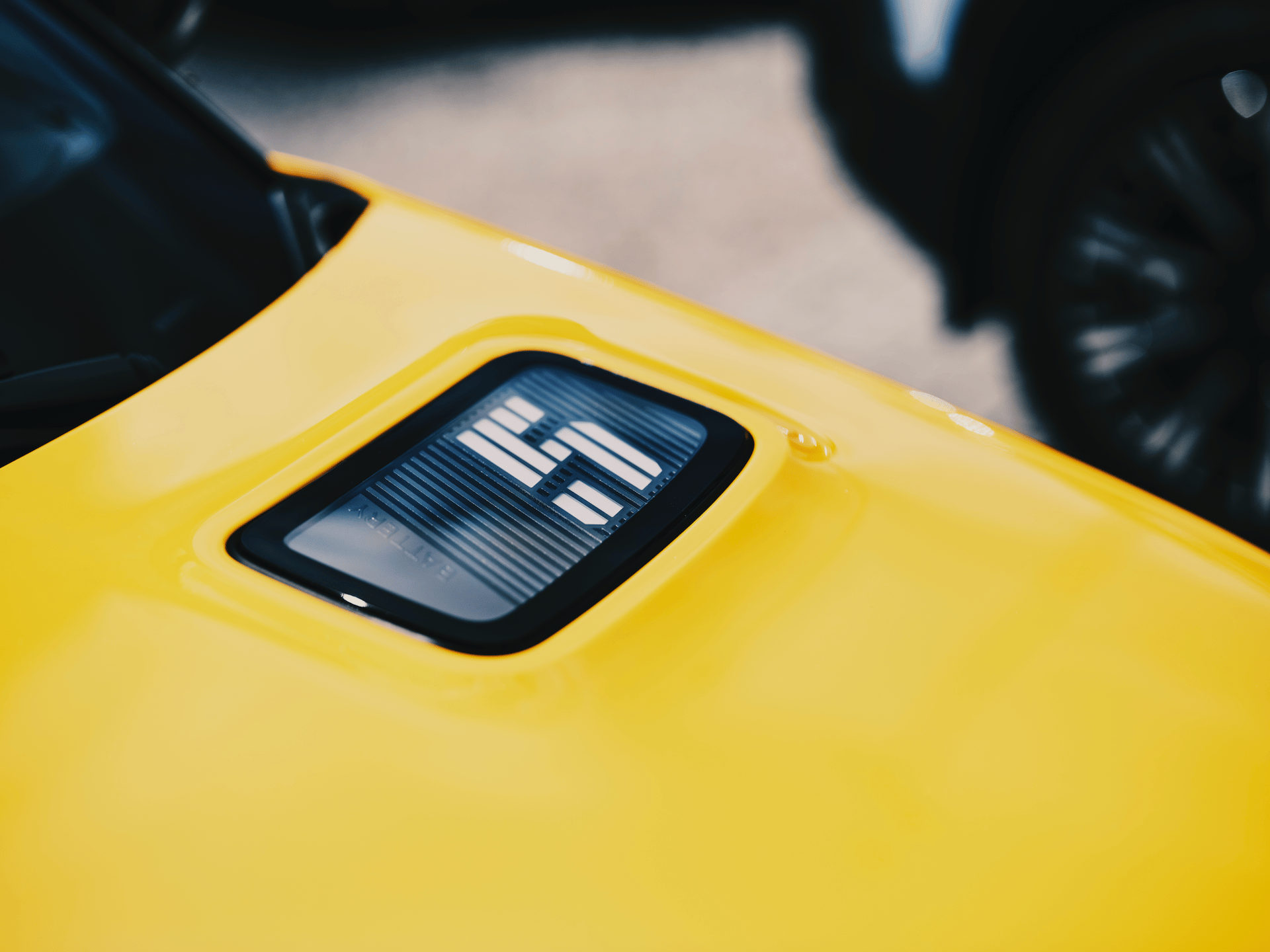 A close-up of a bright yellow car panel featuring a prominent 'HS' or 'LS' emblem or badge.