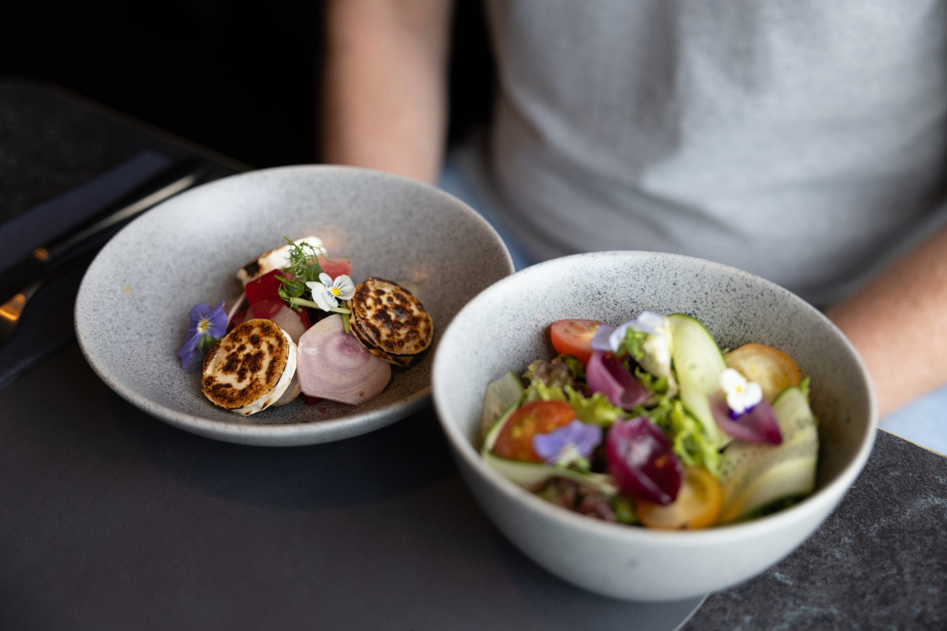 Two bowls of colorful salads with edible flowers on a table, one featuring beets and goat cheese.
