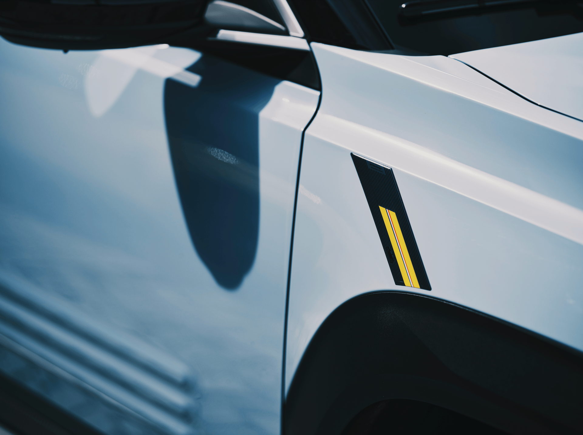 Detail of a white car's front fender featuring a black decal with yellow and red stripes.
