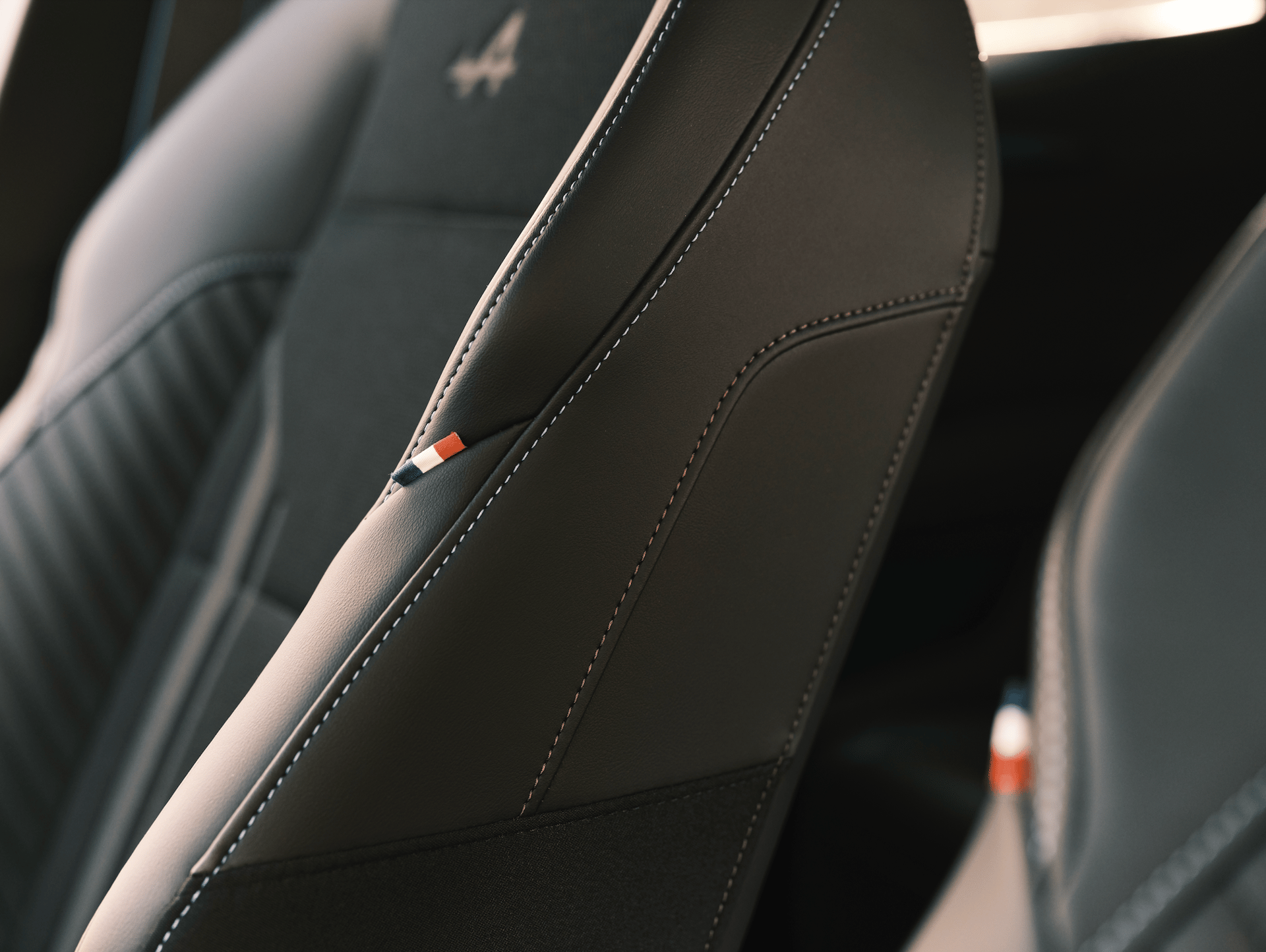 Close-up of a dark leather car seat with white stitching and a small red, white, and blue emblem.