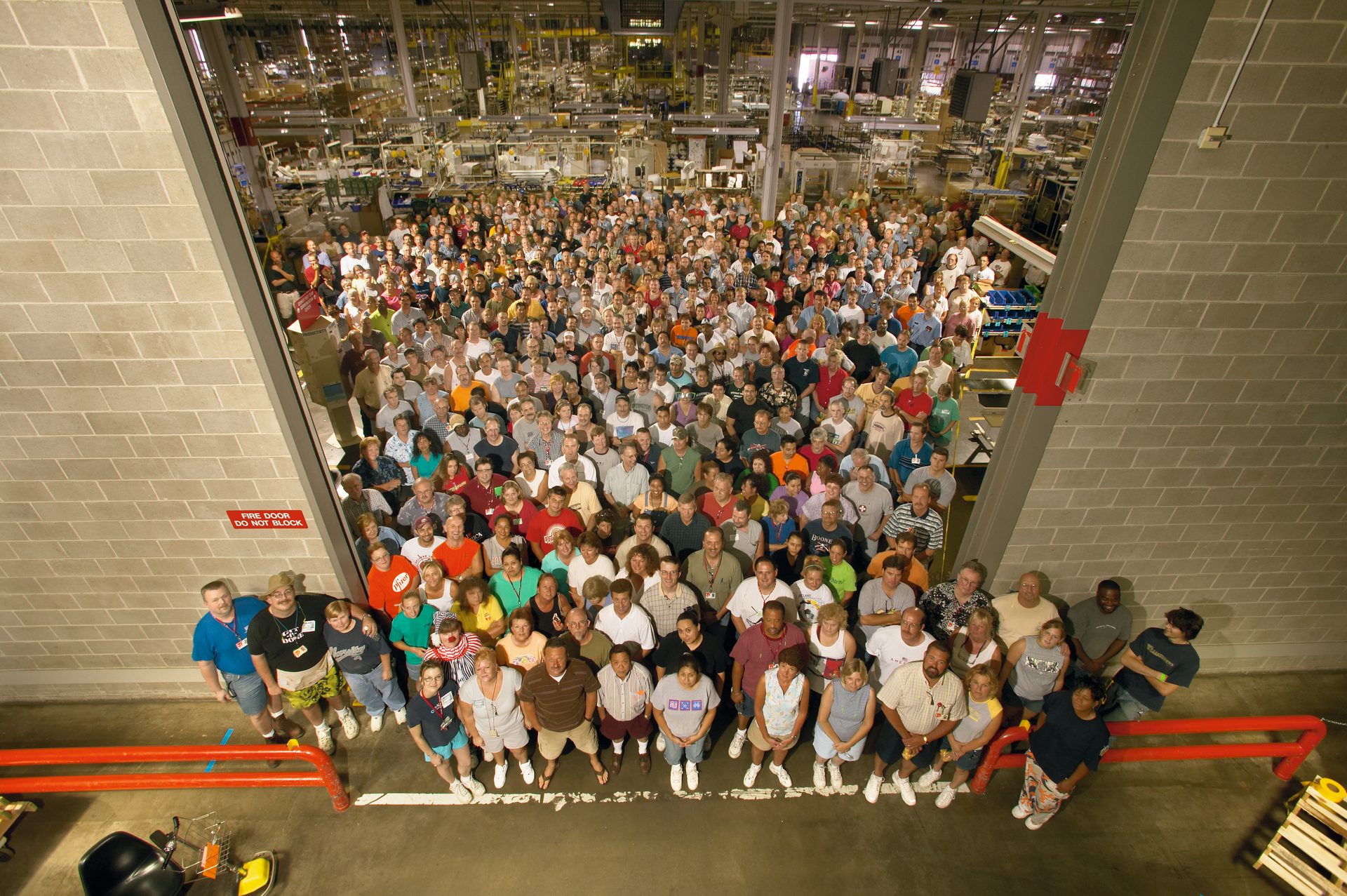 A large crowd of diverse people, seen from above, gathered in a factory or warehouse.