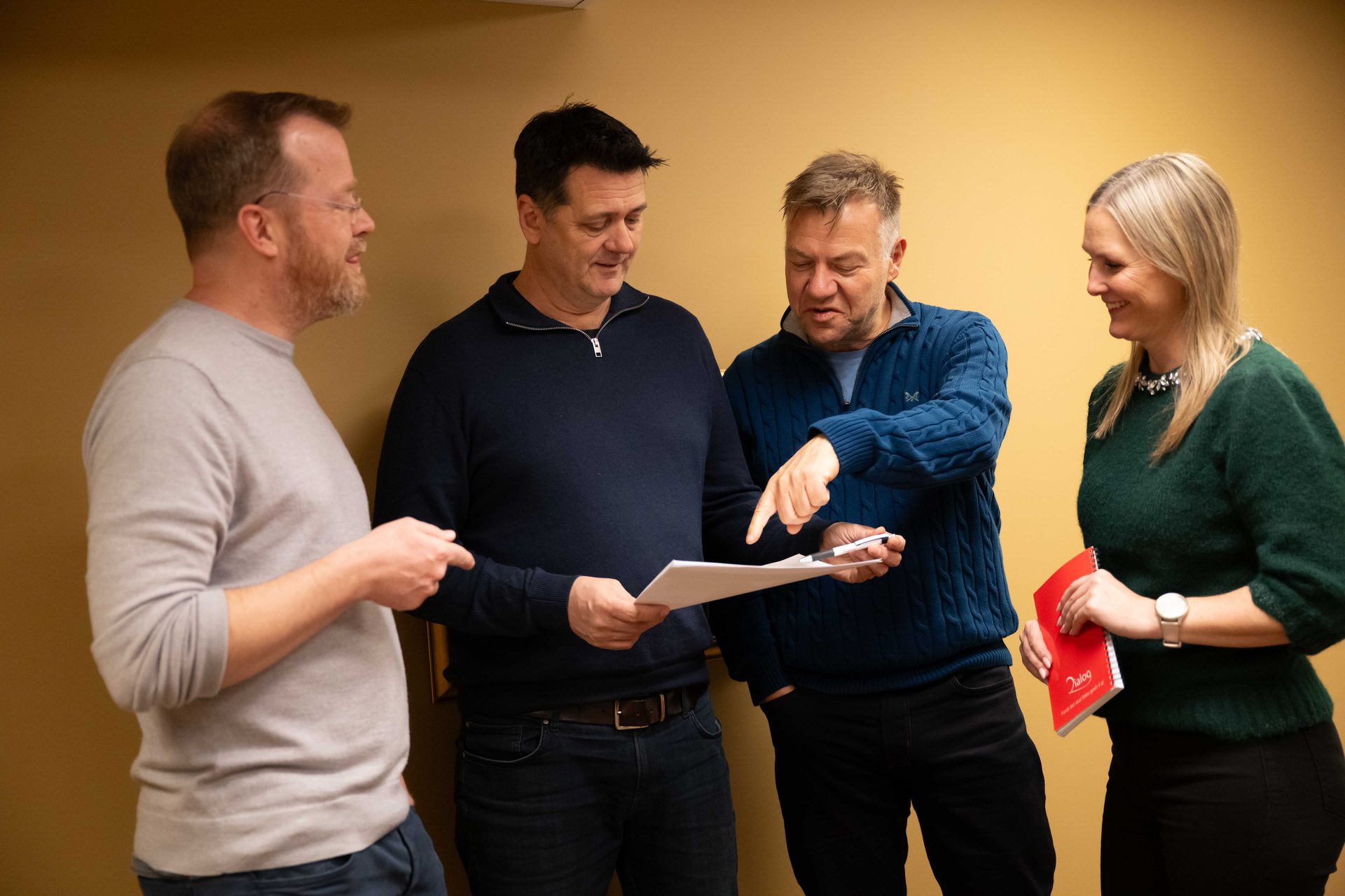 Four colleagues, three men and one woman, discussing documents and pointing at papers during a meeting.