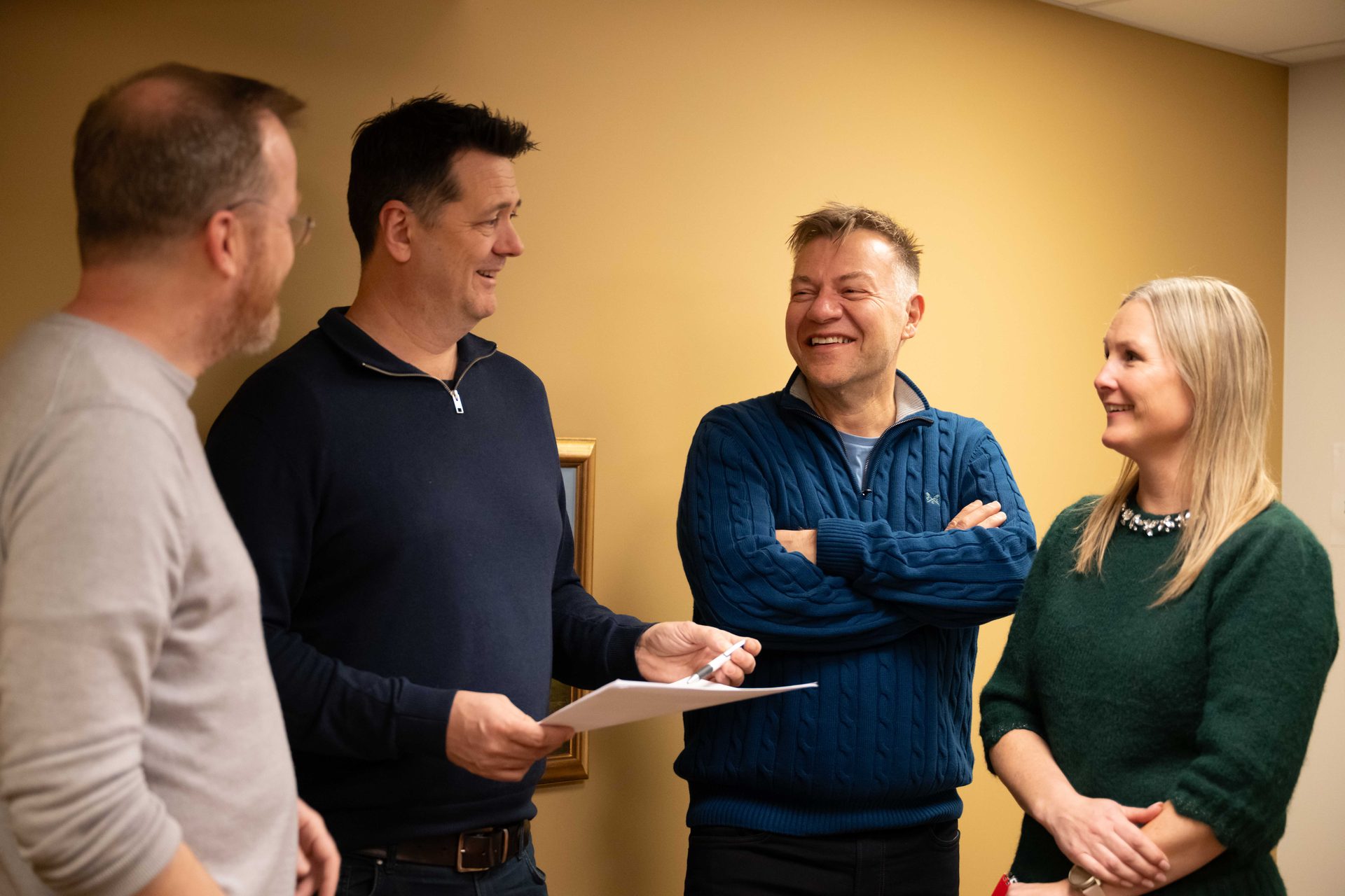 Four colleagues engage in a lively discussion, smiling and sharing ideas in a casual office setting.