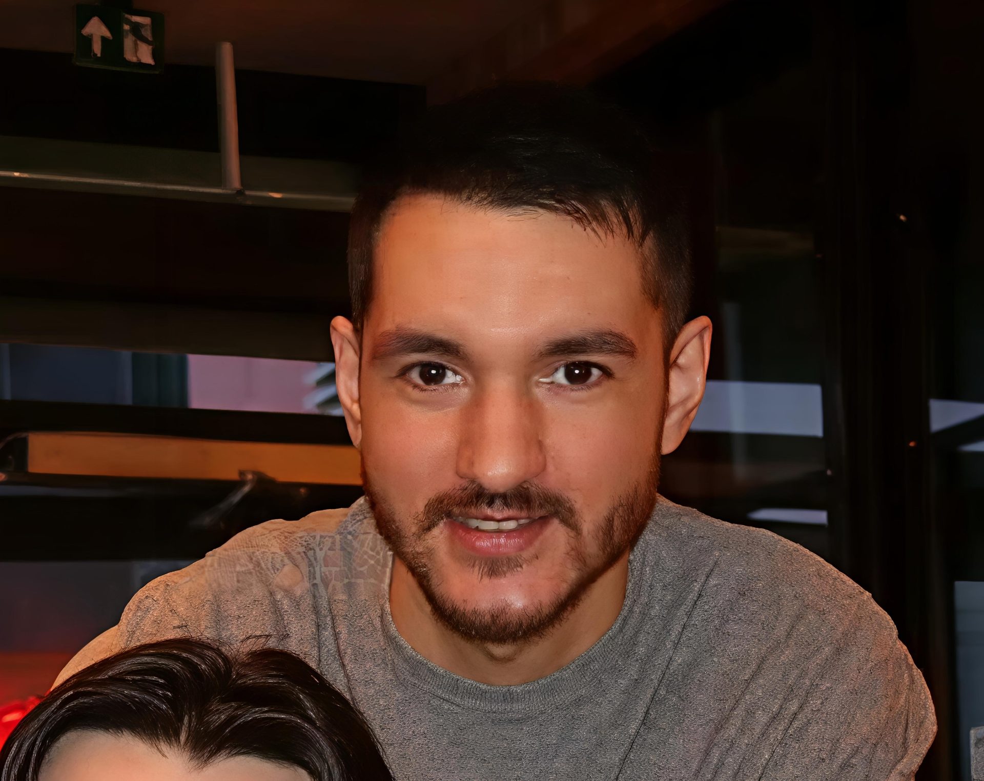 A man with short dark hair and a beard smiles at the camera in an indoor setting.