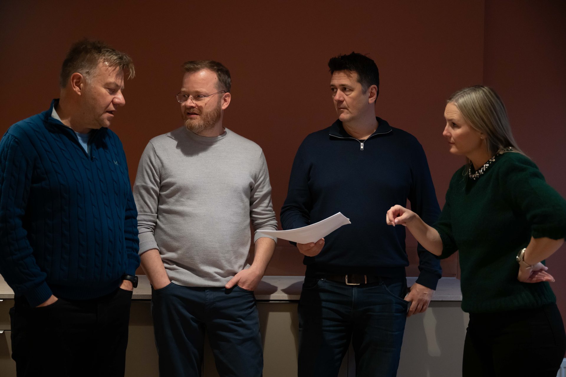 Four colleagues, three men and one woman, stand in a line, engaged in a discussion.