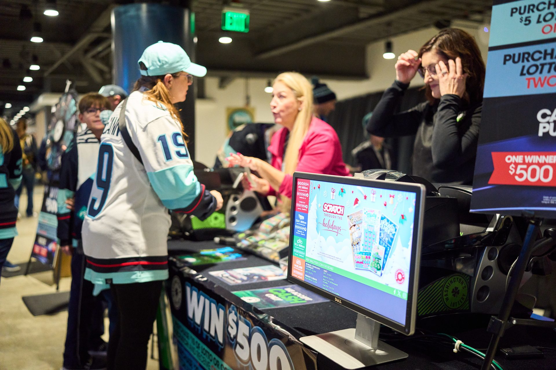 People at a Washington's Lottery booth, with a monitor showing holiday-themed scratch tickets.