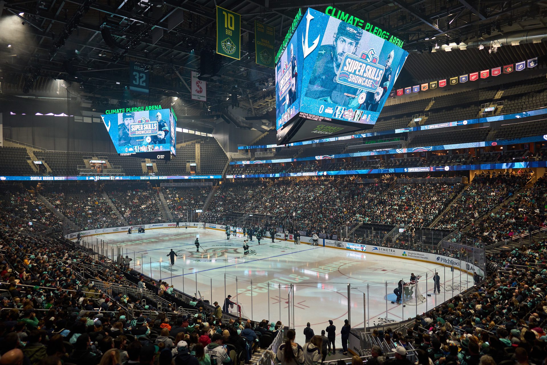 Crowded Climate Pledge Arena during a hockey event, with "Super Skills Showcase" on jumbotron.