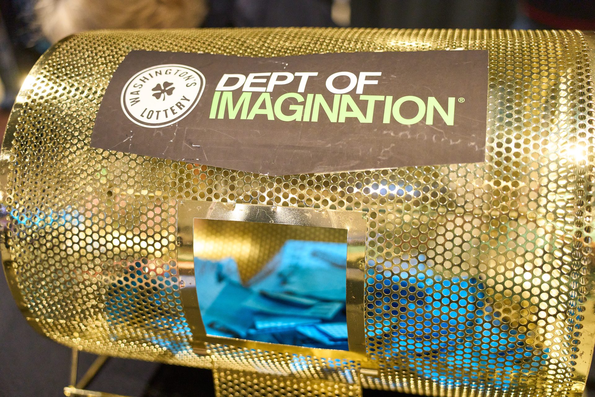 Golden lottery drum with blue tickets, labeled "Washington's Lottery Dept of Imagination".