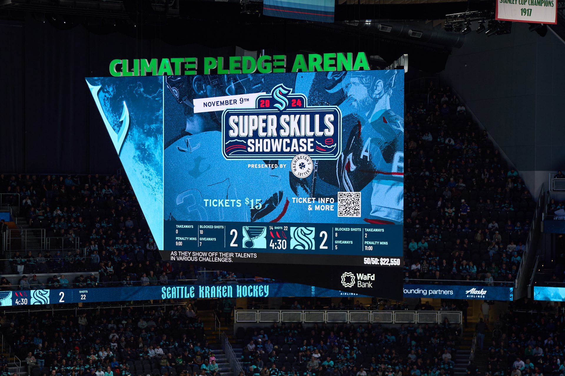 Large jumbotron in Climate Pledge Arena showing a "Super Skills Showcase" ad and a 2-2 hockey score.