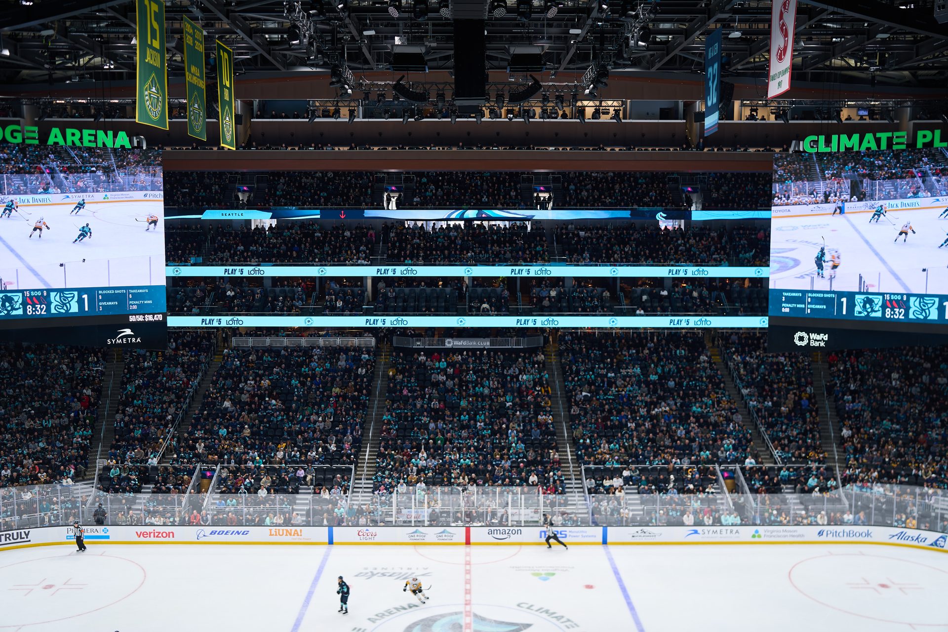 Indoor ice hockey game in a large arena with spectators, video screens, and banners.