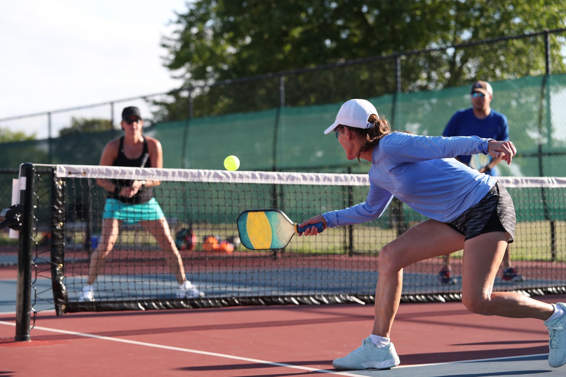 People playing pickleball on a court, a woman in the foreground hitting the ball.