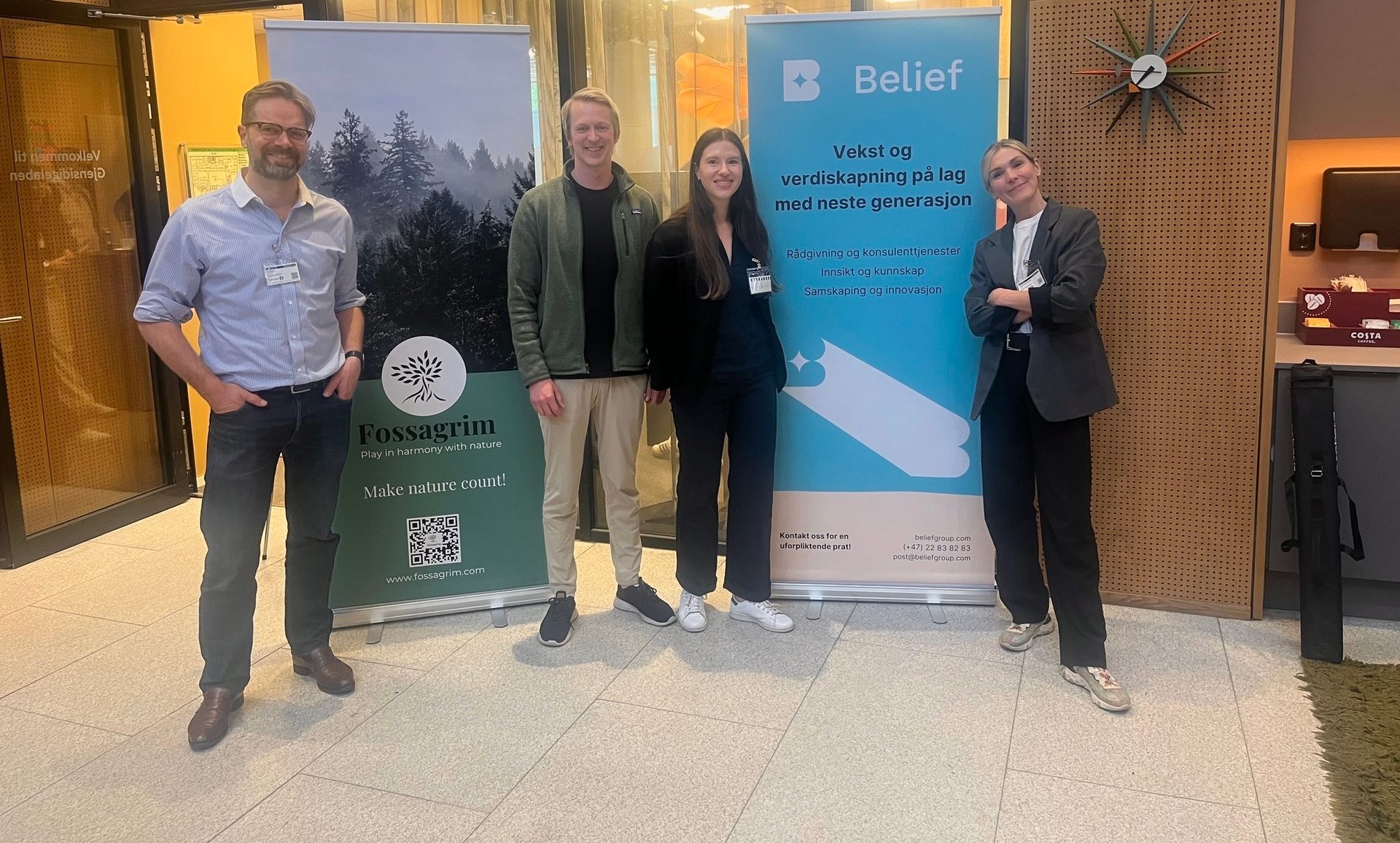 Four people standing by "Fossagrim" and "Belief" company banners.