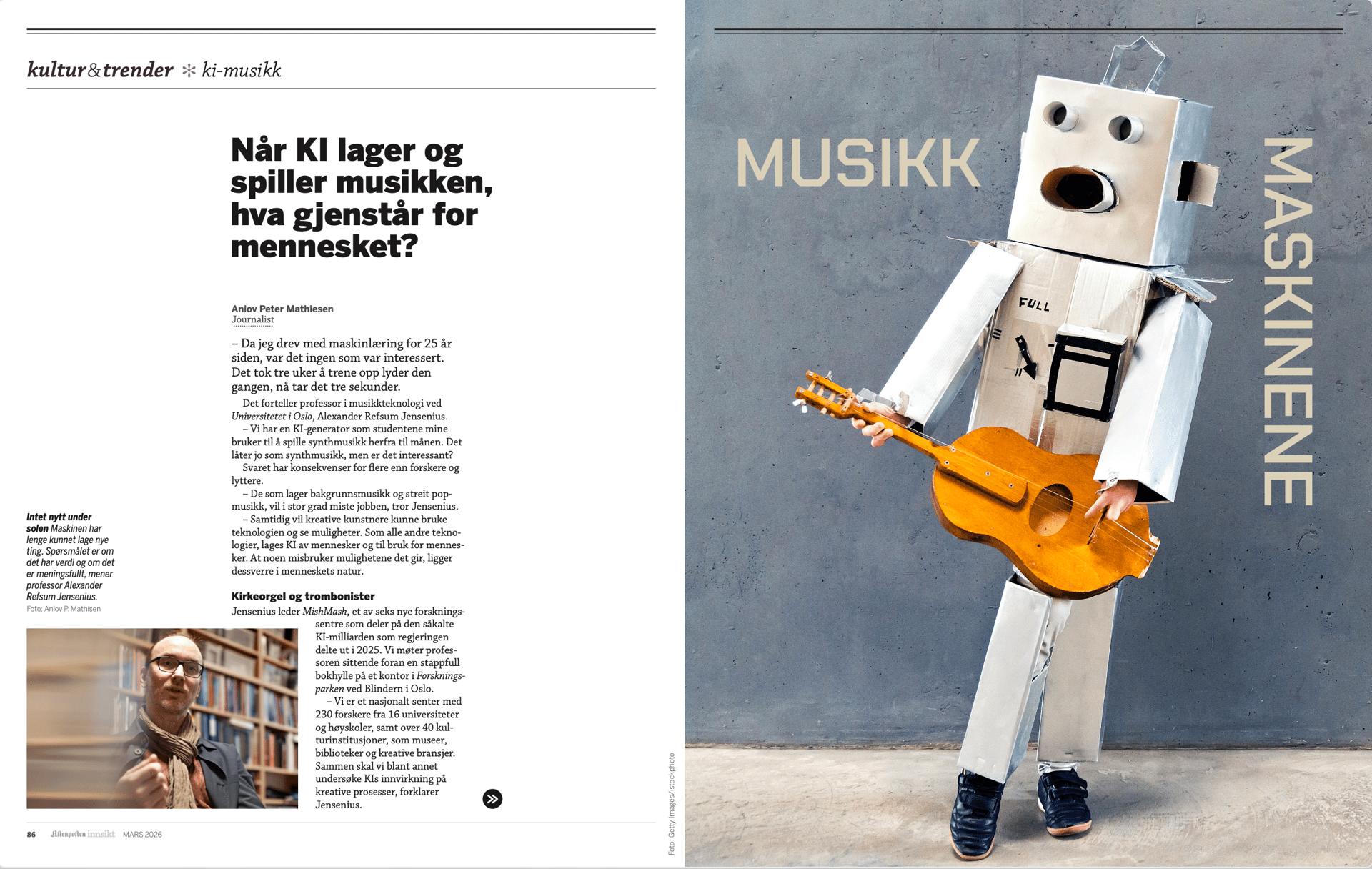 A cardboard robot dressed in white, holding and playing a wooden guitar against a concrete wall.