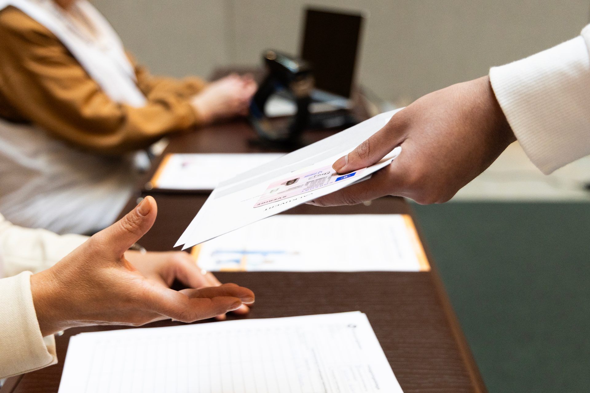 Hands exchanging an ID card or driver's license across a desk.