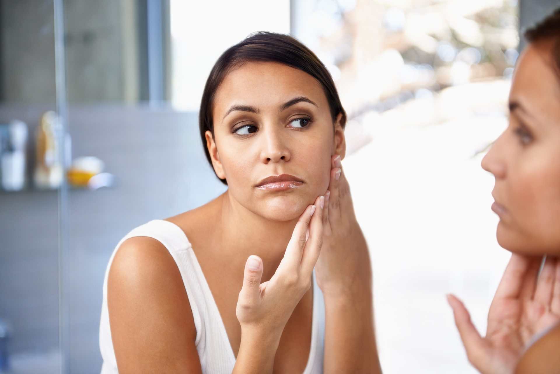 Woman looking intently at her reflection in a mirror, touching her face.