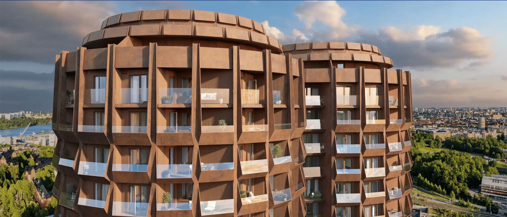 Two unique, round, brown buildings with balconies, overlooking a city and green landscape.