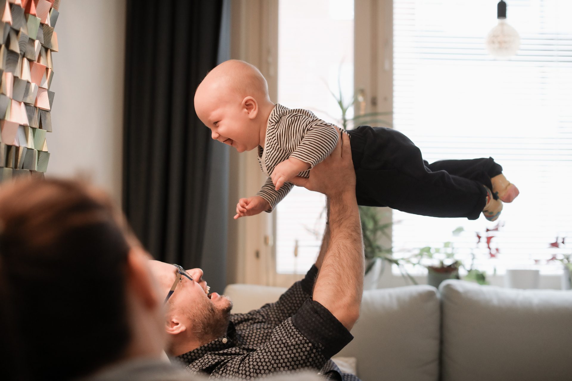 Father holds a laughing baby high in the air.