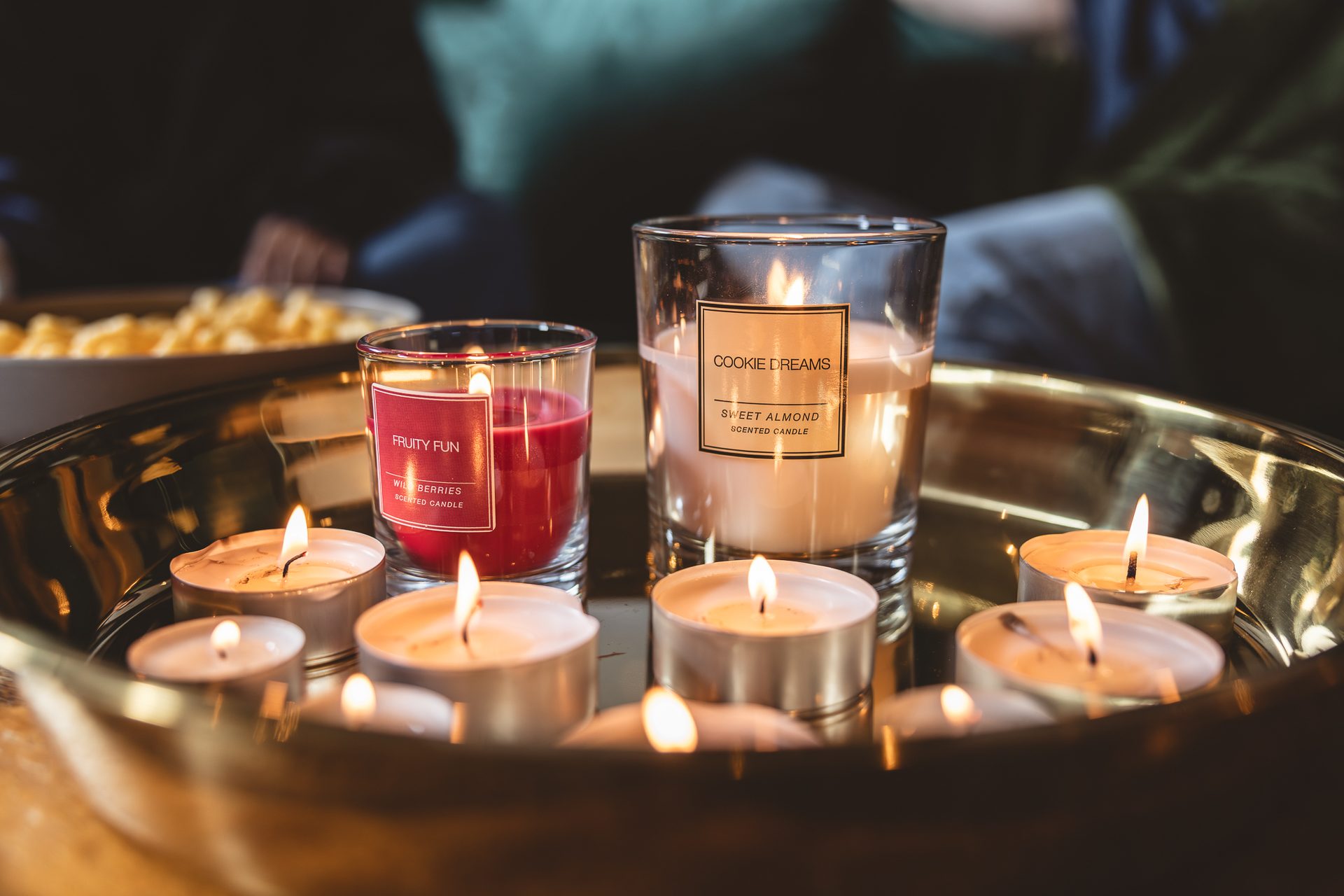 Golden tray with lit scented candles and tea lights, a bowl of snacks blurred in the background.