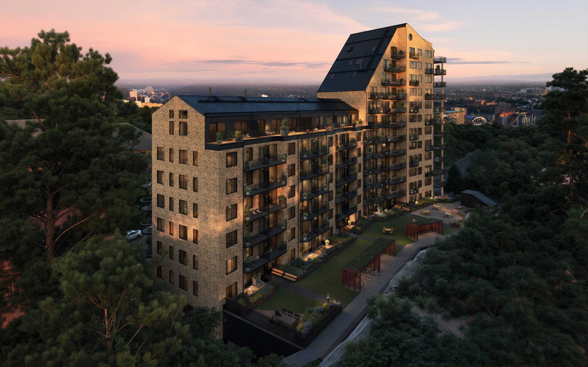 Contemporary brick apartment building nestled in trees, overlooking a city at sunset.