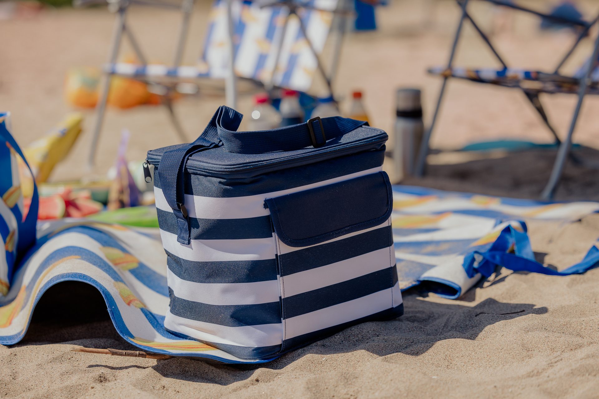 Close-up of a blue and white striped cooler bag and beach mat on sand.