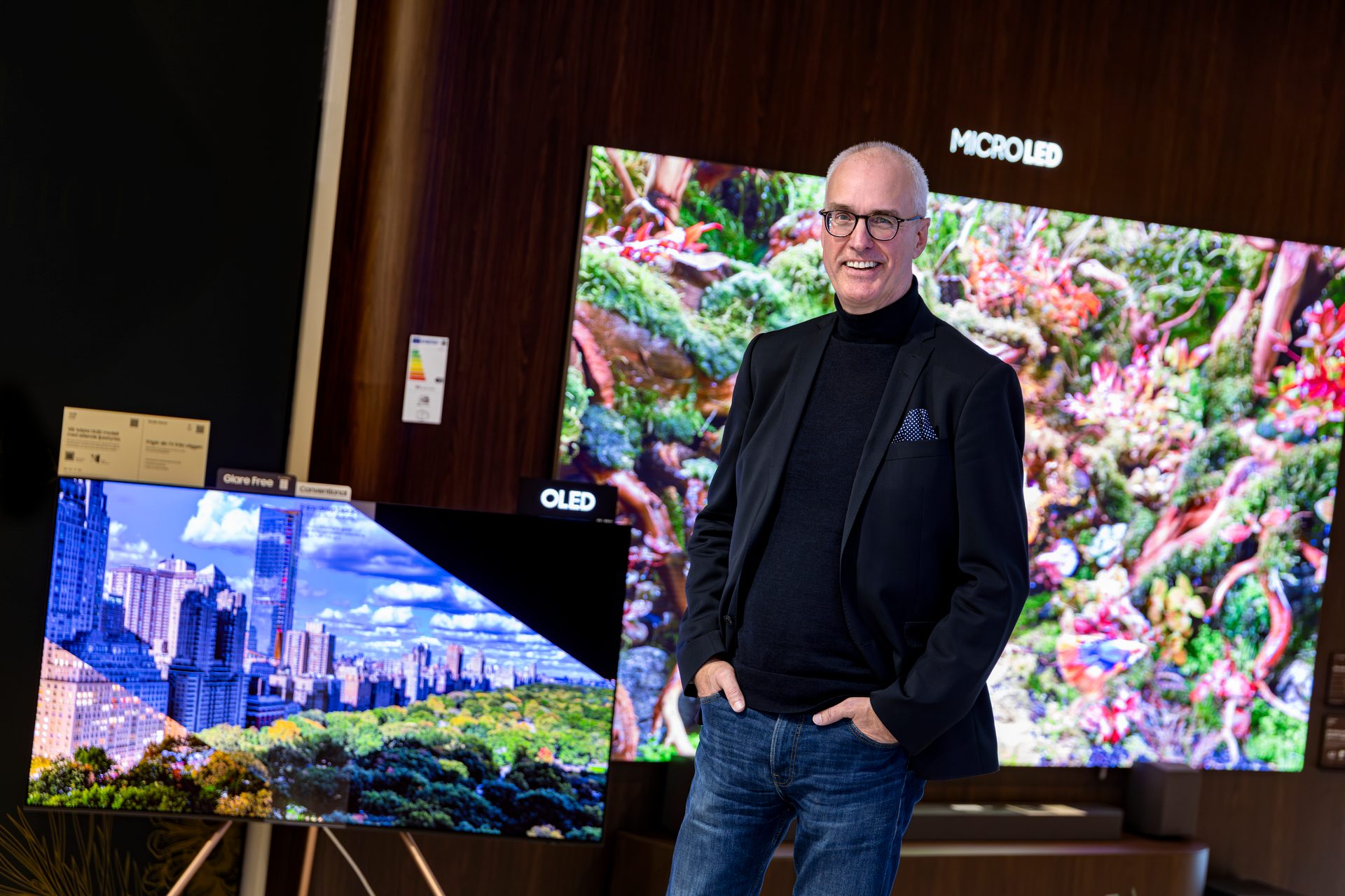 Smiling man in front of large screens, labeled "OLED" and "MICROLED."