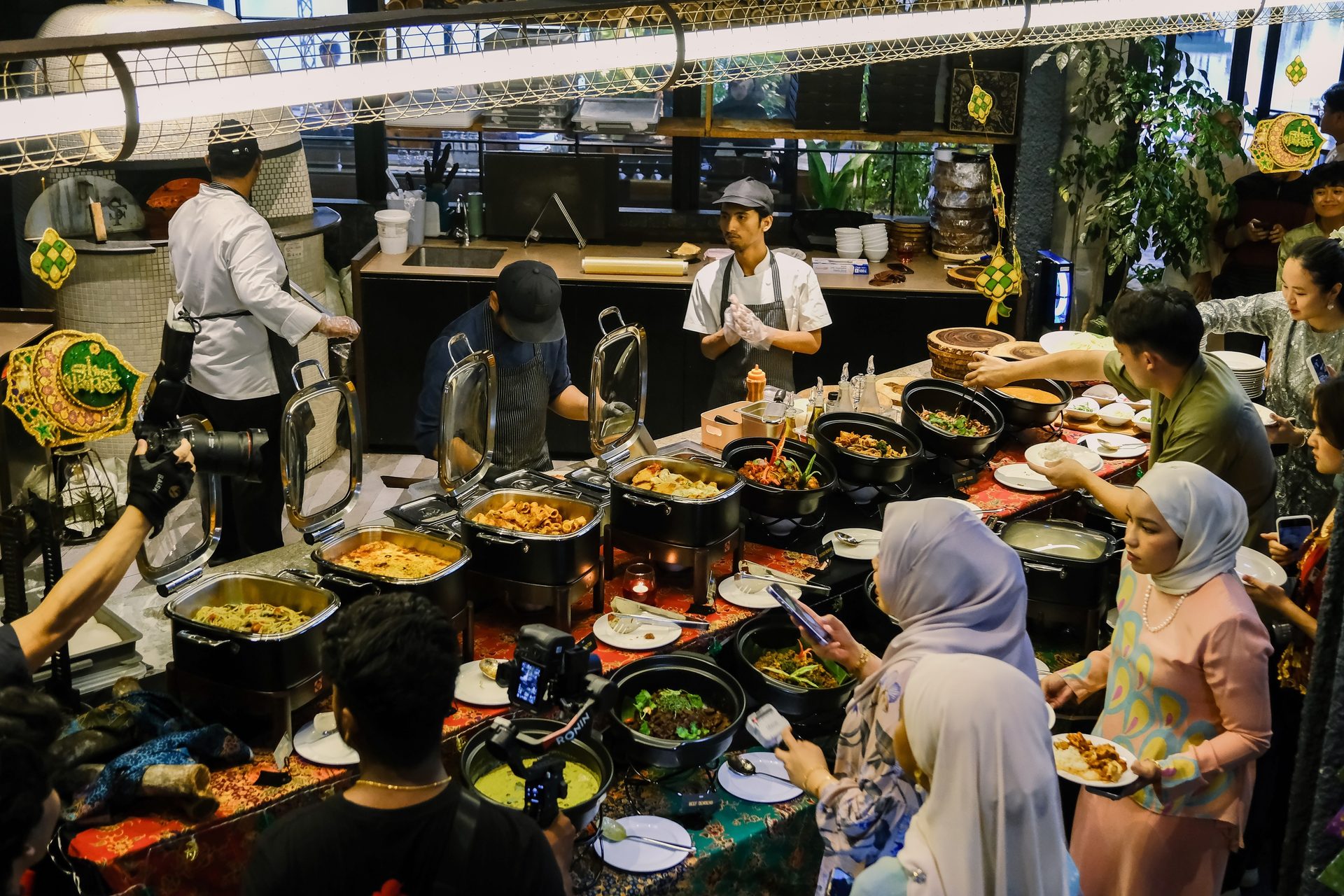 A busy restaurant buffet line with people serving food, and chefs working in the background.