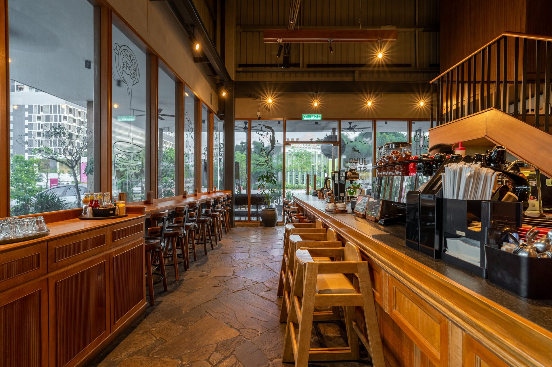 Interior of a cafe with a long counter, bar stools, and large windows overlooking an urban area.