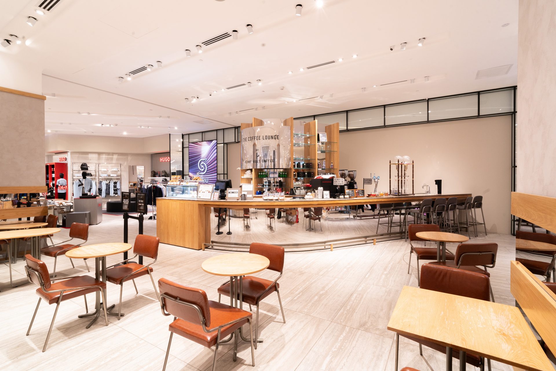 Modern coffee lounge with seating and a counter in a bright retail store with clothing sections nearby.