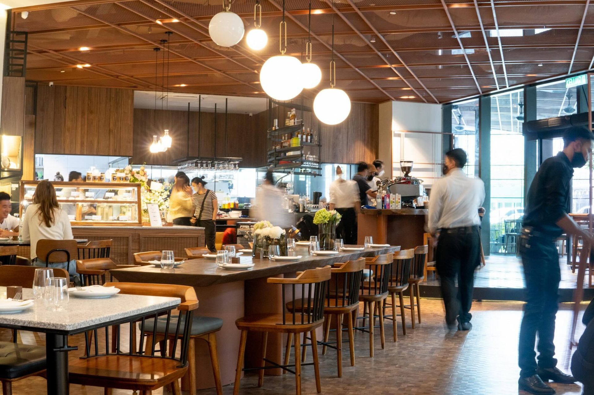 Modern restaurant interior with wooden decor, dining tables, globe lights, and blurred people.