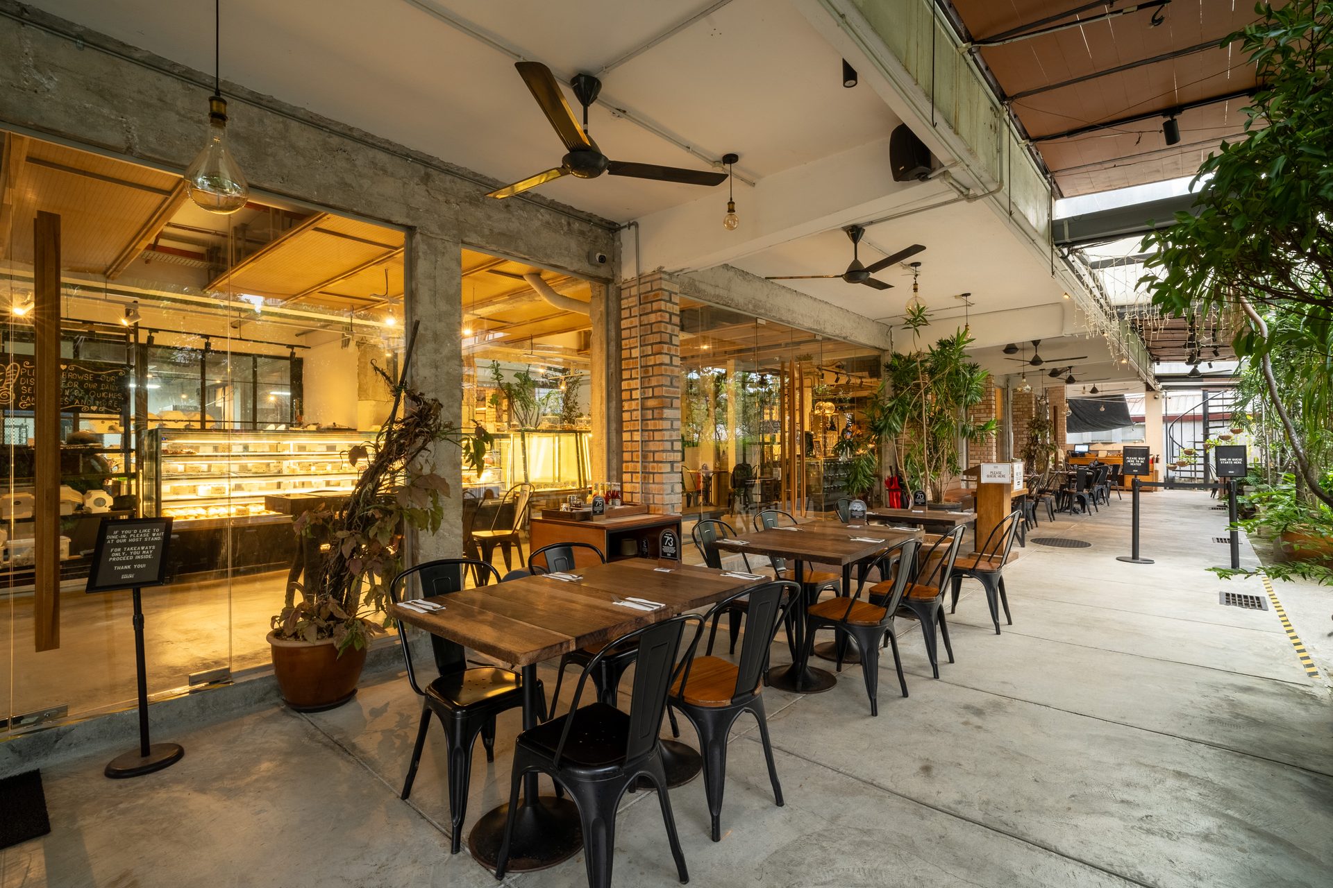 Cafe outdoor patio with wooden tables, chairs, glass facade showing bakery inside.