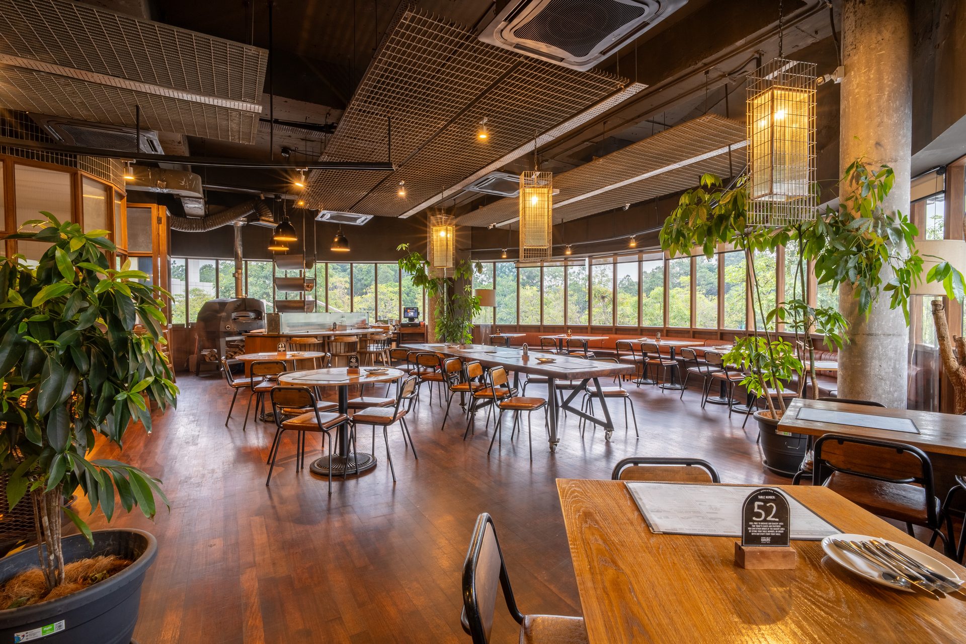 A spacious restaurant interior with wooden floors, many tables, large windows, and a mesh ceiling.