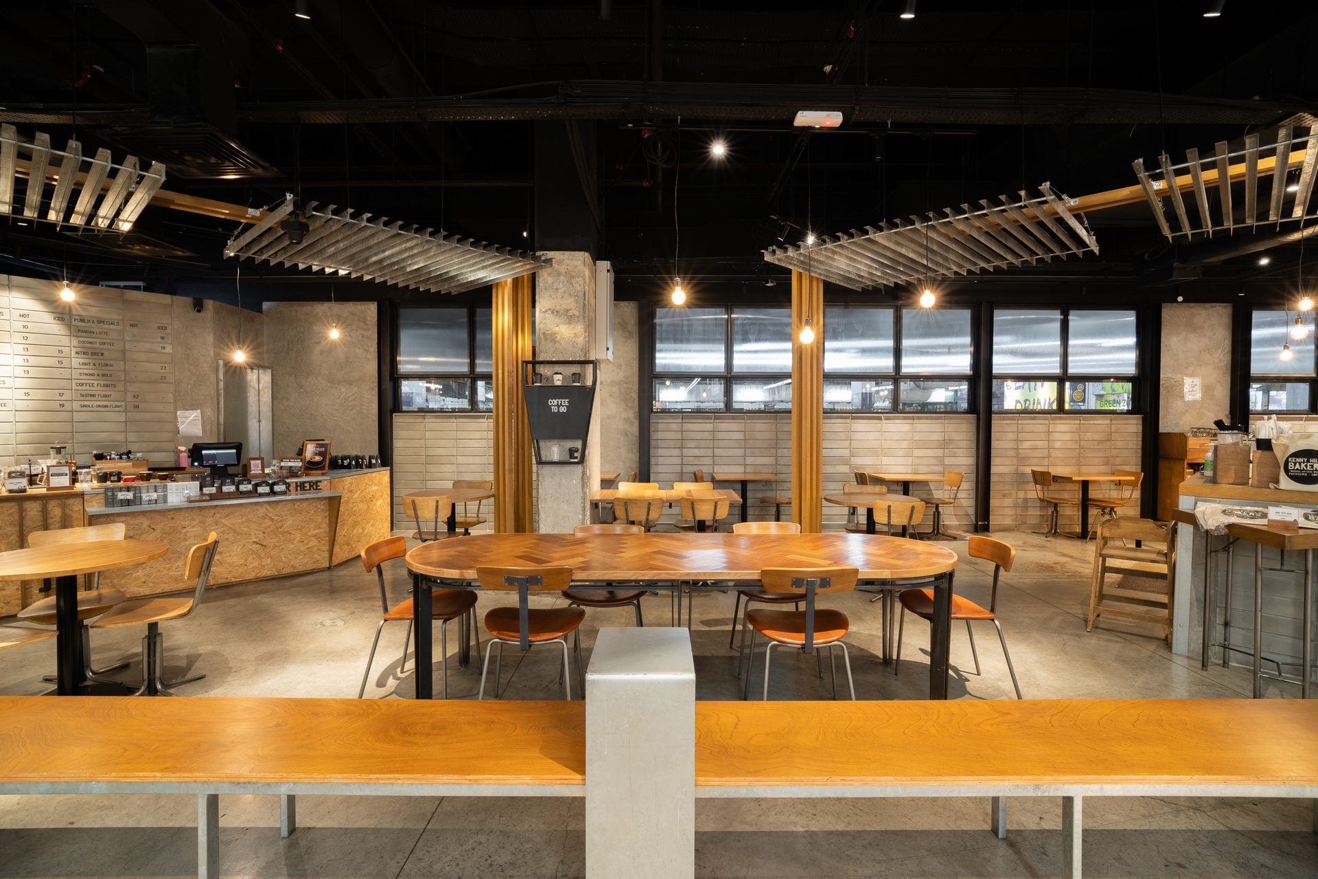 Spacious, industrial-style cafe interior with wooden tables, a large communal table, and a service counter.