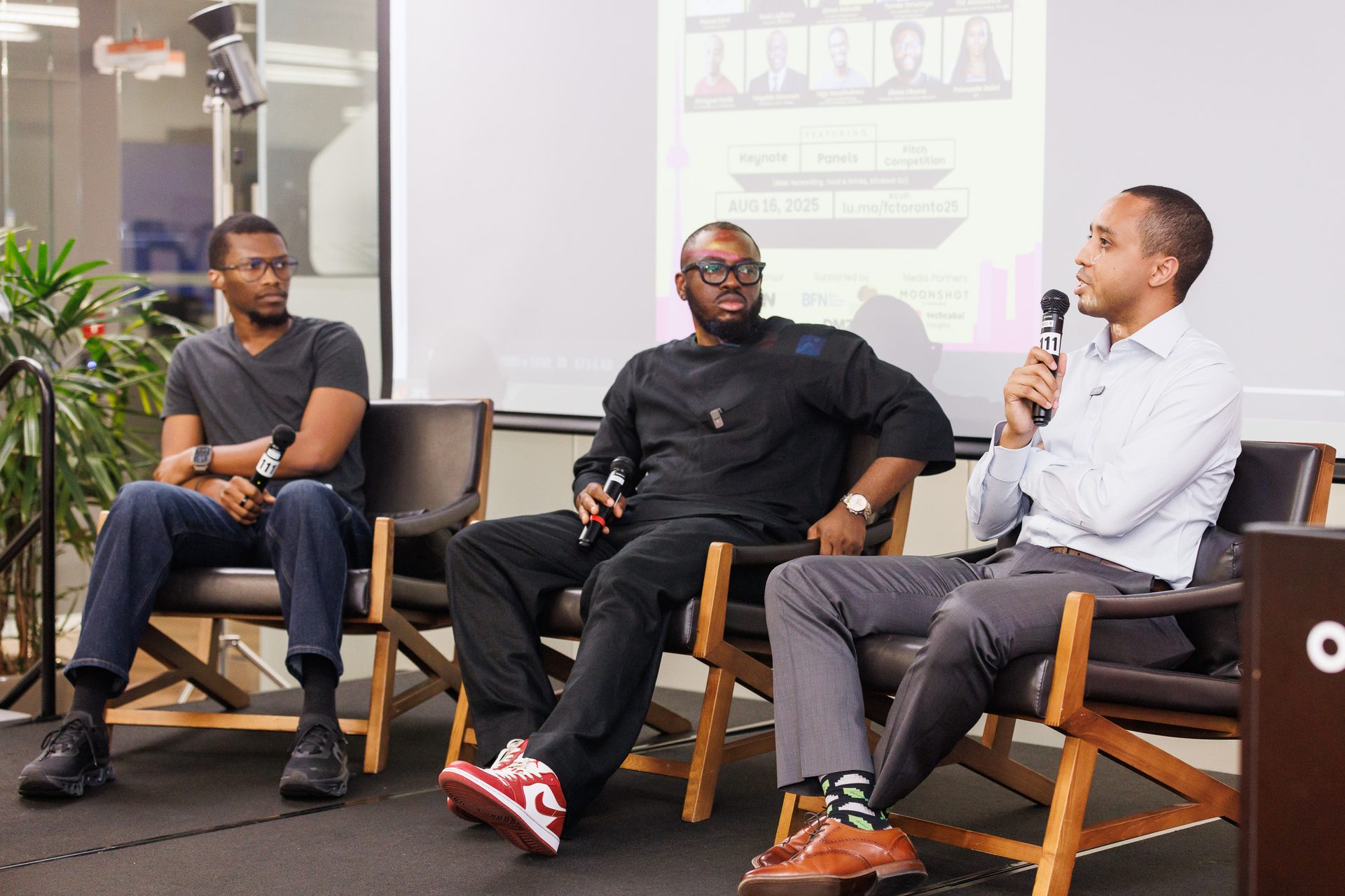 Three men on stage with microphones, engaged in a panel discussion at an event.