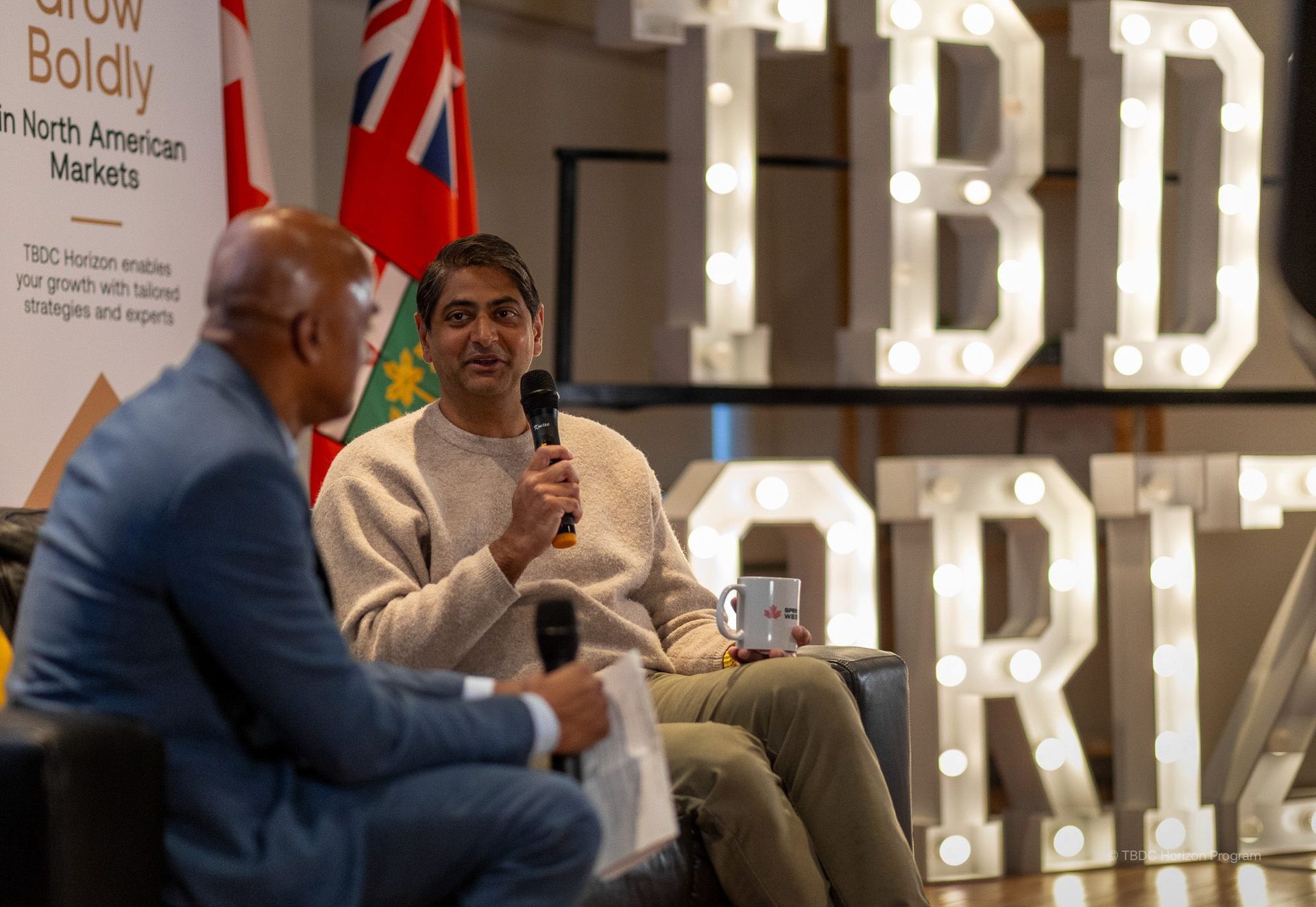 Two men on a panel, one speaking into a microphone, with "TBDC Horizon" branding.
