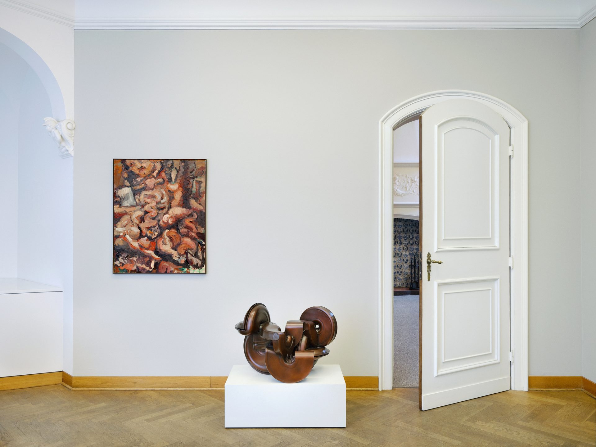 Modern art display: painting, abstract sculpture, open arched door to another room.