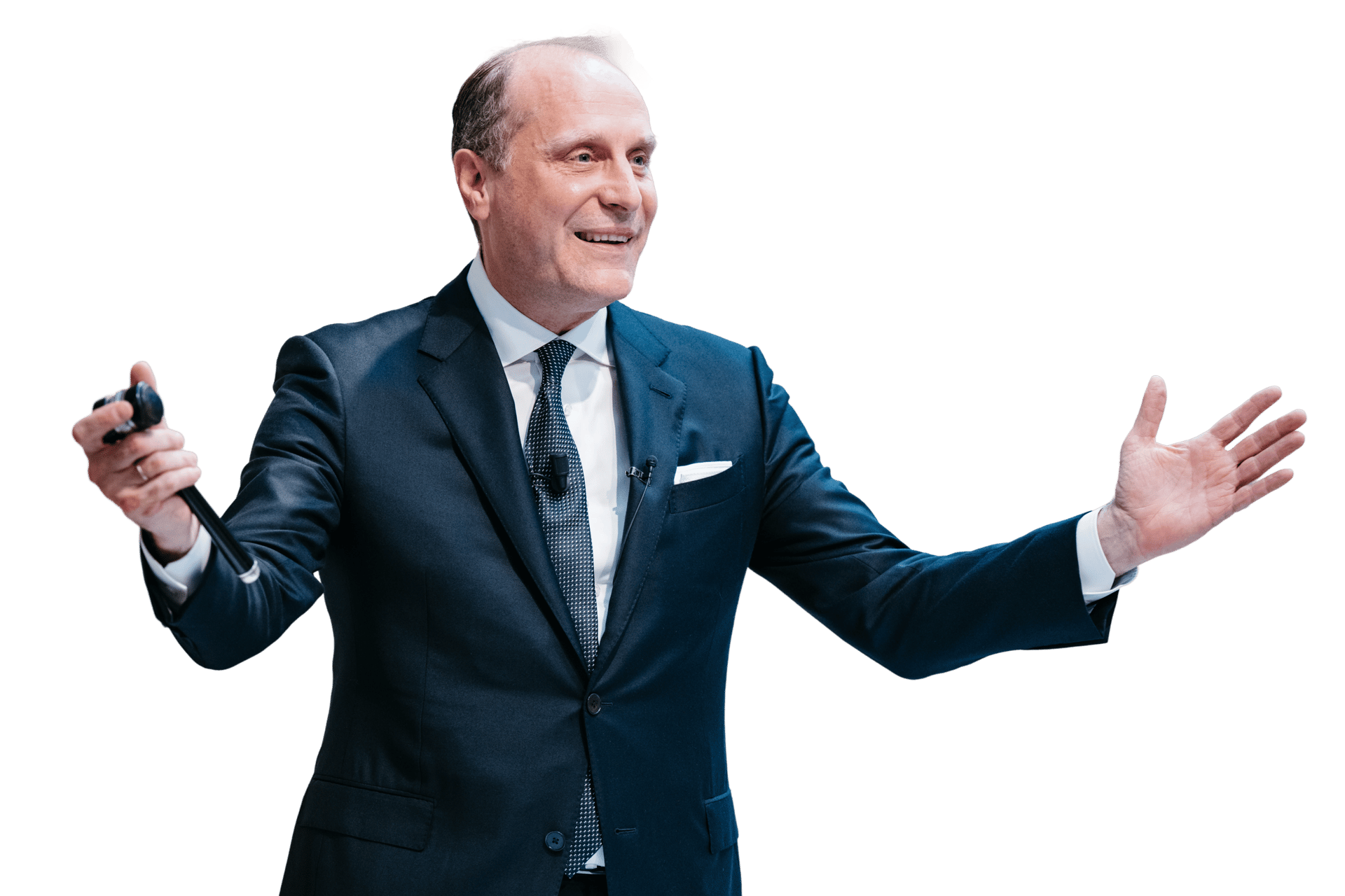 Smiling man in a dark suit holds a microphone and gestures with an open hand.