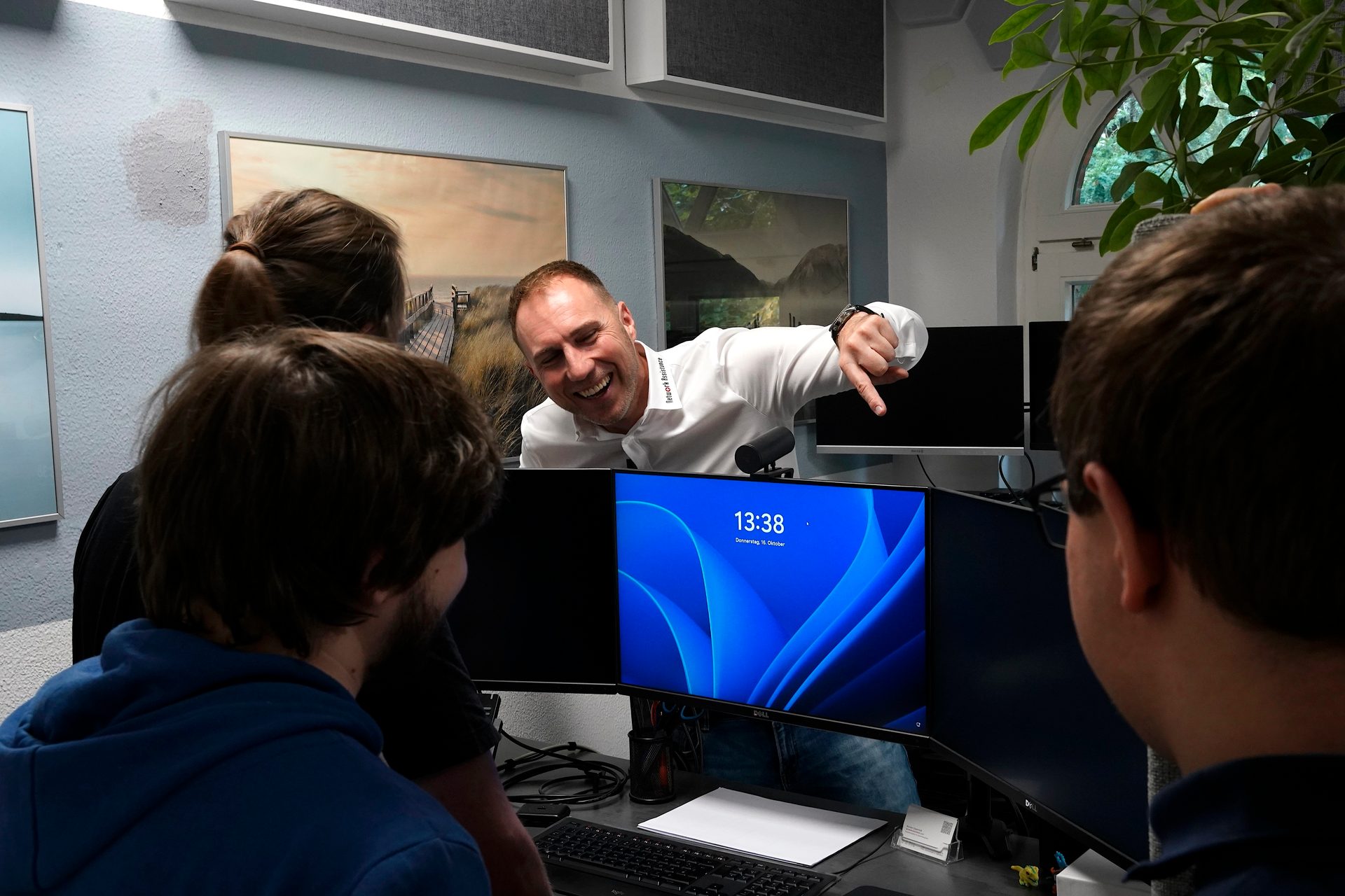 Smiling man points at a monitor displaying 13:38 to a group of people.