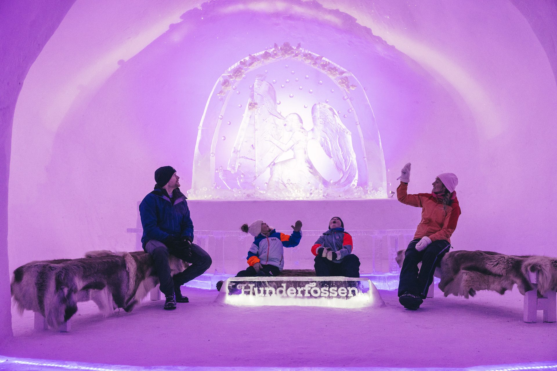 People in a purple-lit ice structure with ice sculptures, including "Hunderfossen" text.