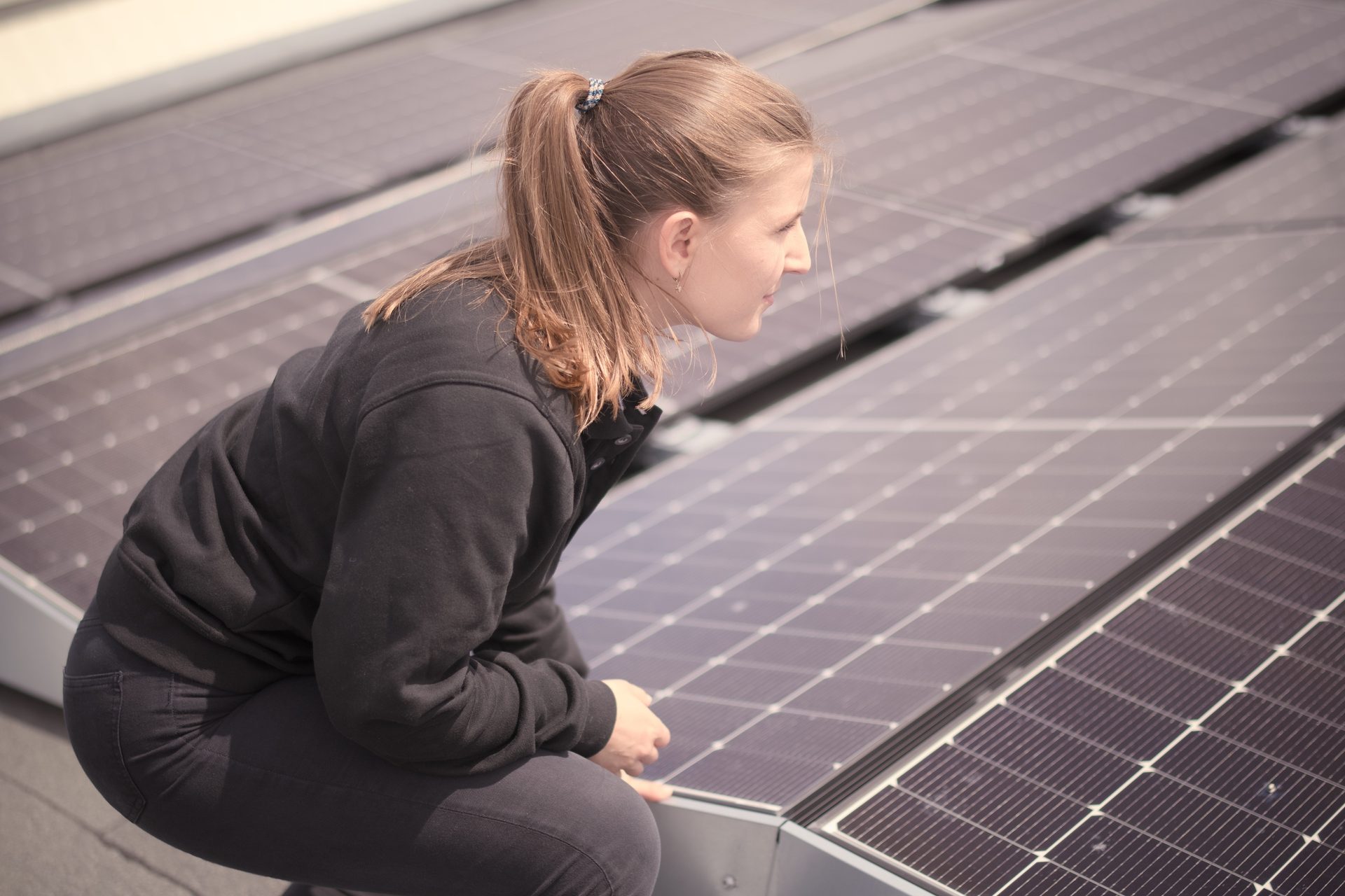 A young woman crouching on a rooftop, inspecting or working on solar panels.