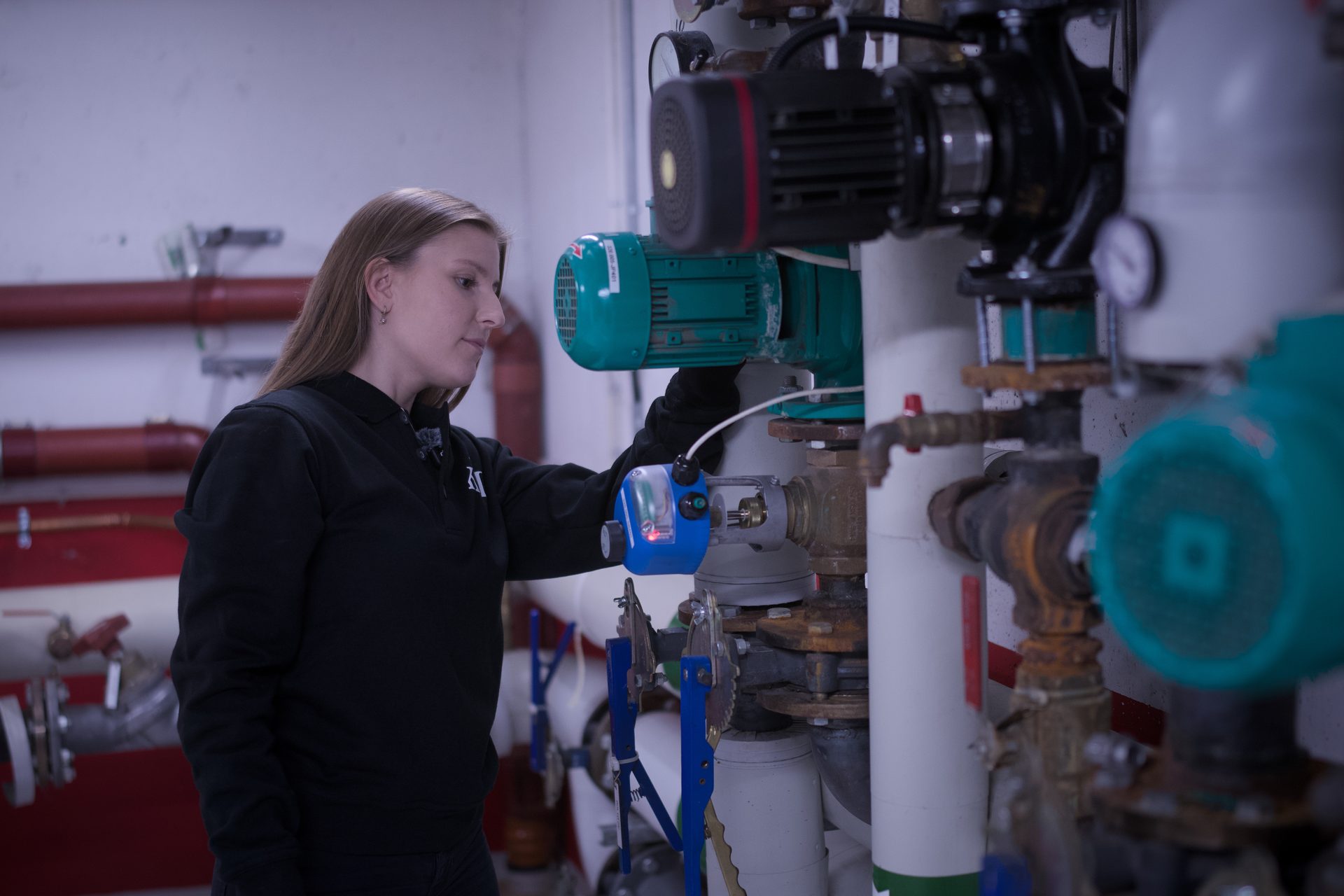 A woman in a black uniform inspecting industrial machinery with a handheld device.