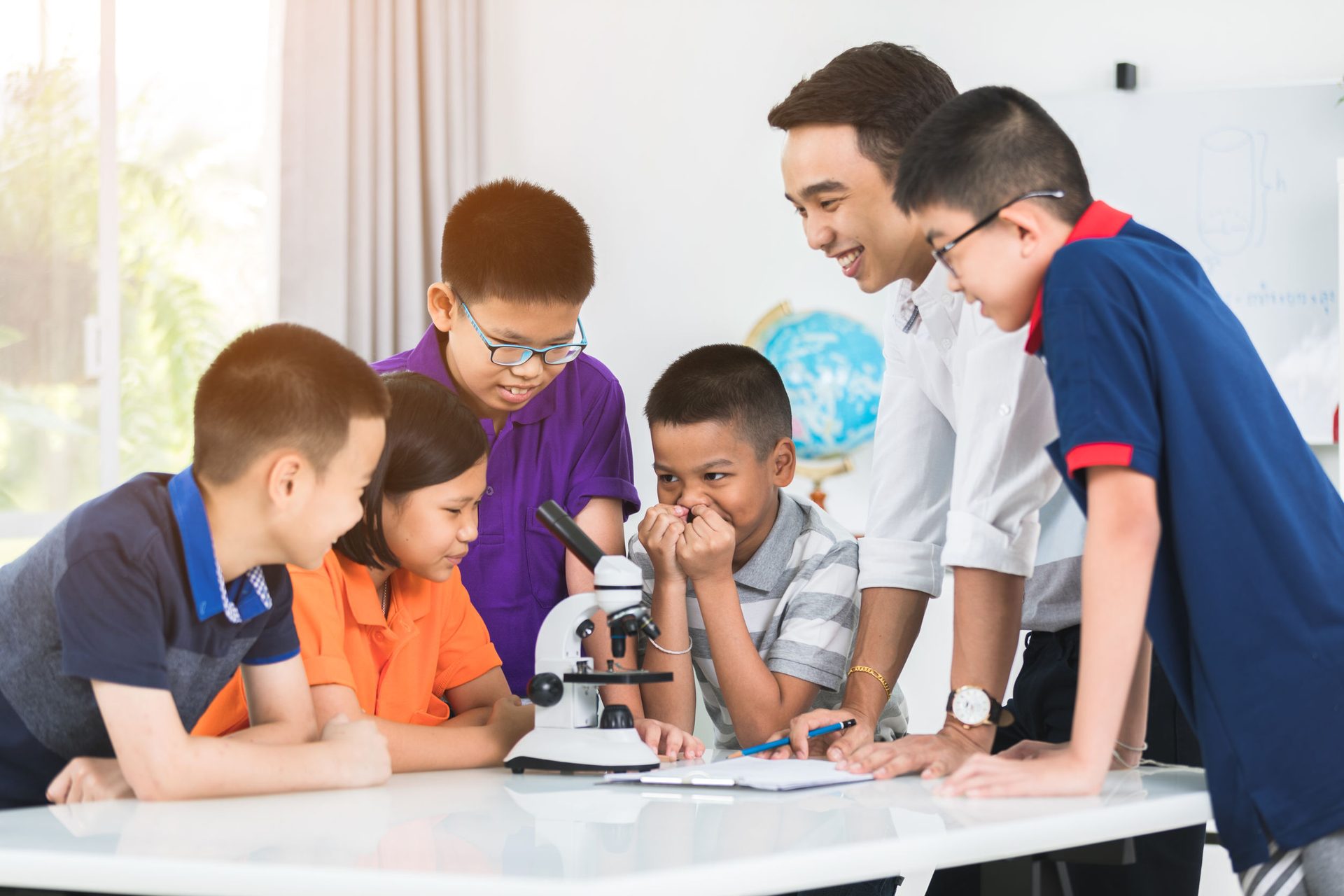 Teacher and students use a microscope in a bright classroom.