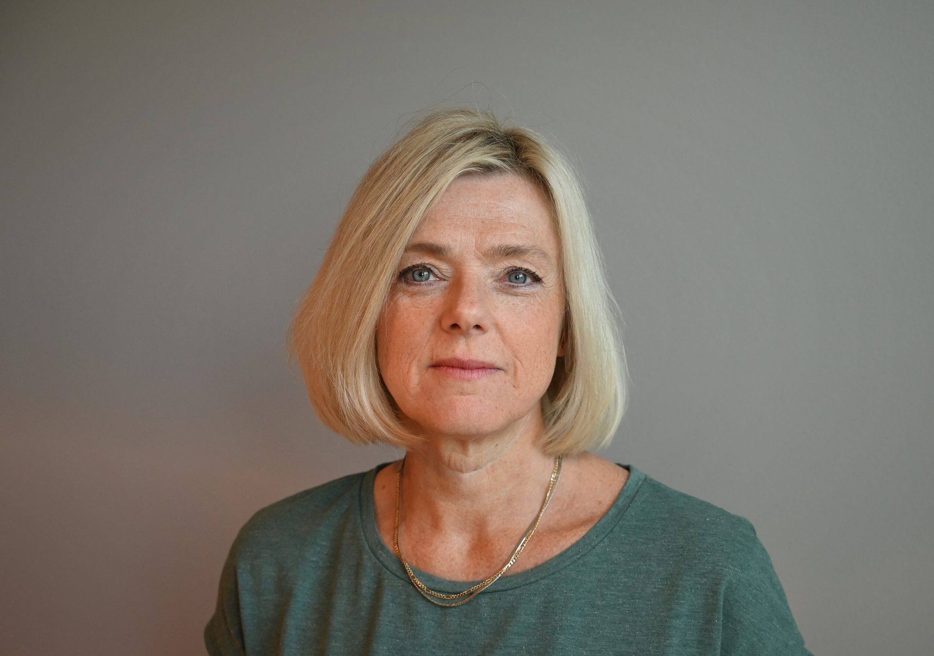 Headshot of a middle-aged woman with blonde hair and blue eyes, wearing a green top.